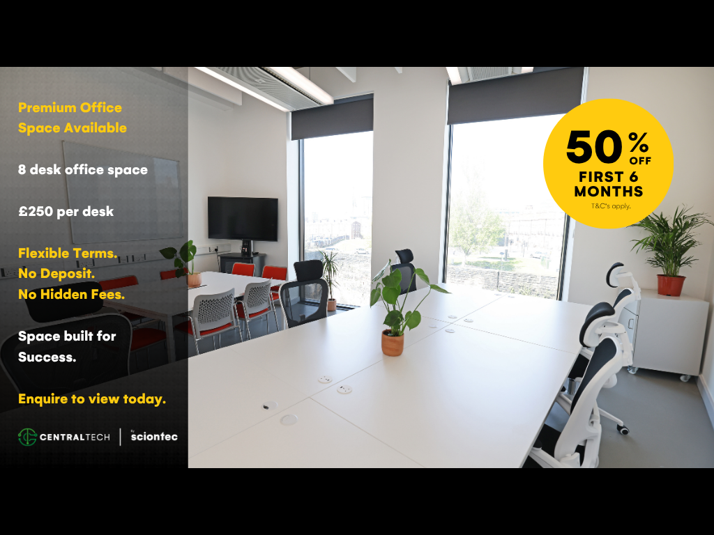 Office workspace with four people working at desks in a bright room with large windows and plants.