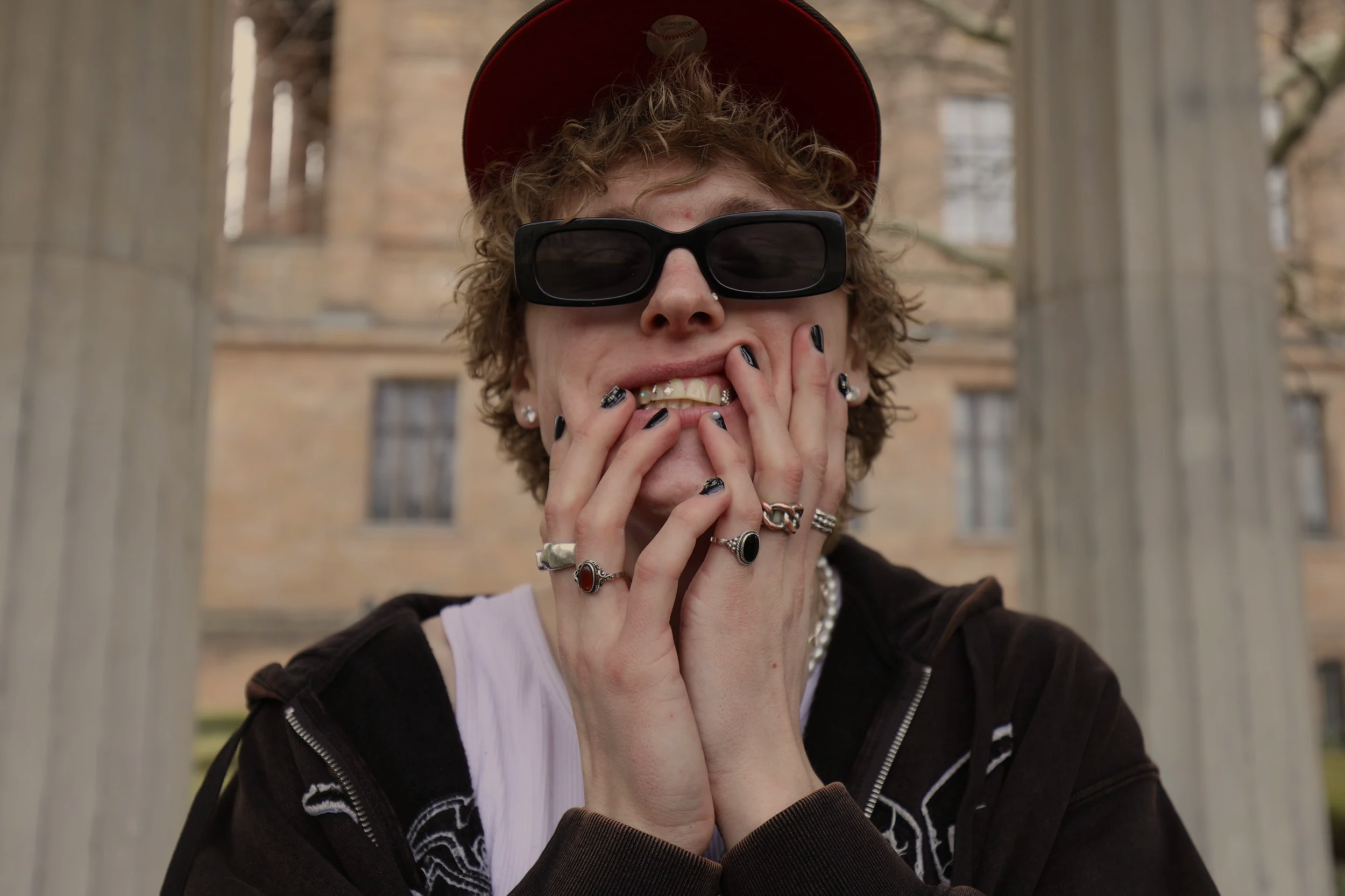 White blonde Swedish man with sunglasses, jewelry and grills holding his face while smiling