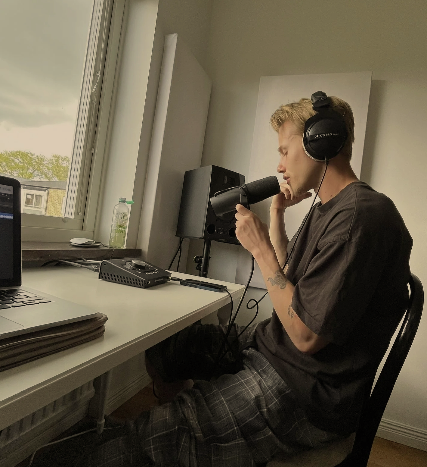 Blonde man sitting in a room and recording vocals for music