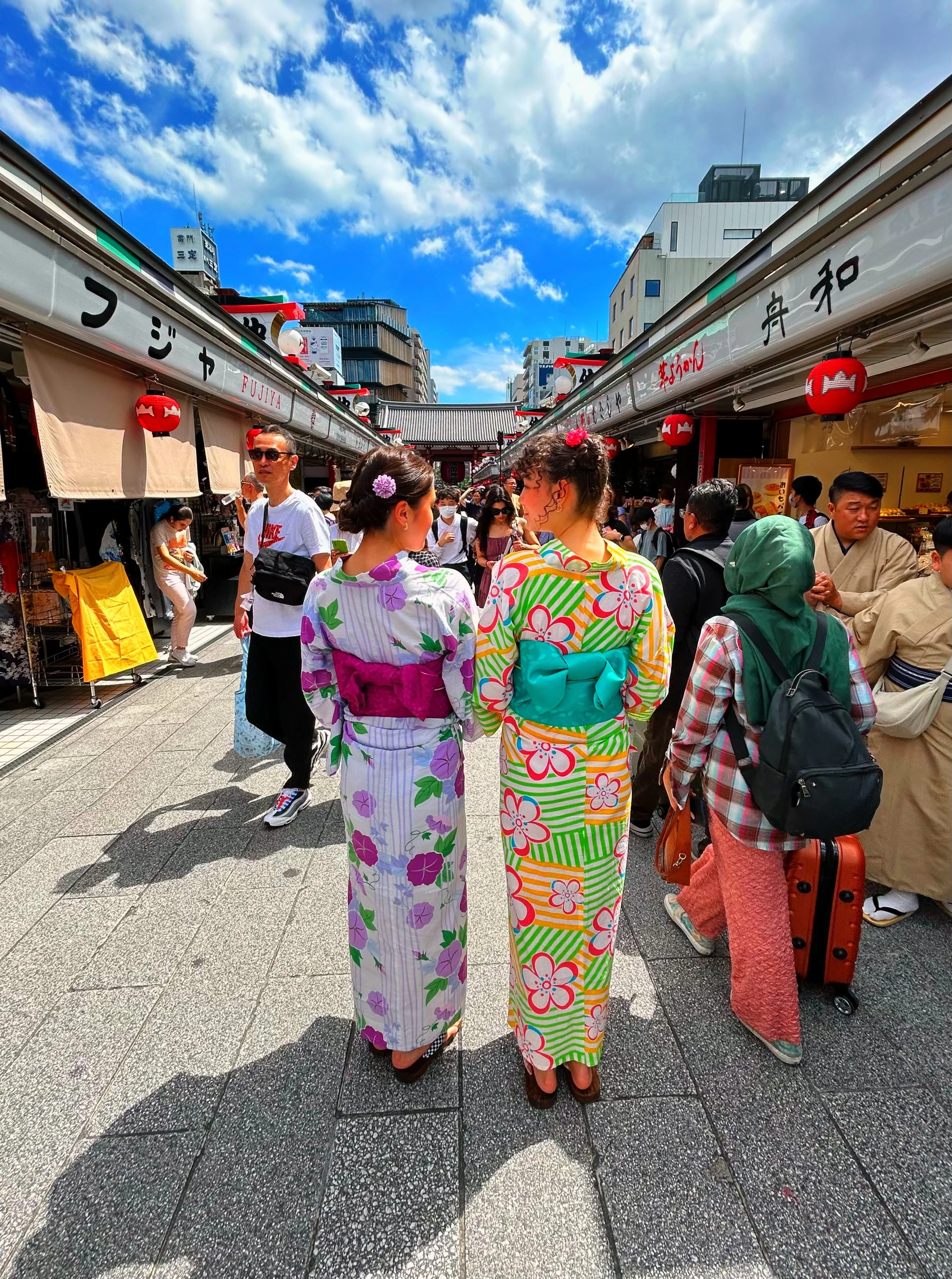 Miri and Esther wear colorful yukata standing in Asakusa, Japan on a sunny day with blue skies and scattered clouds.
