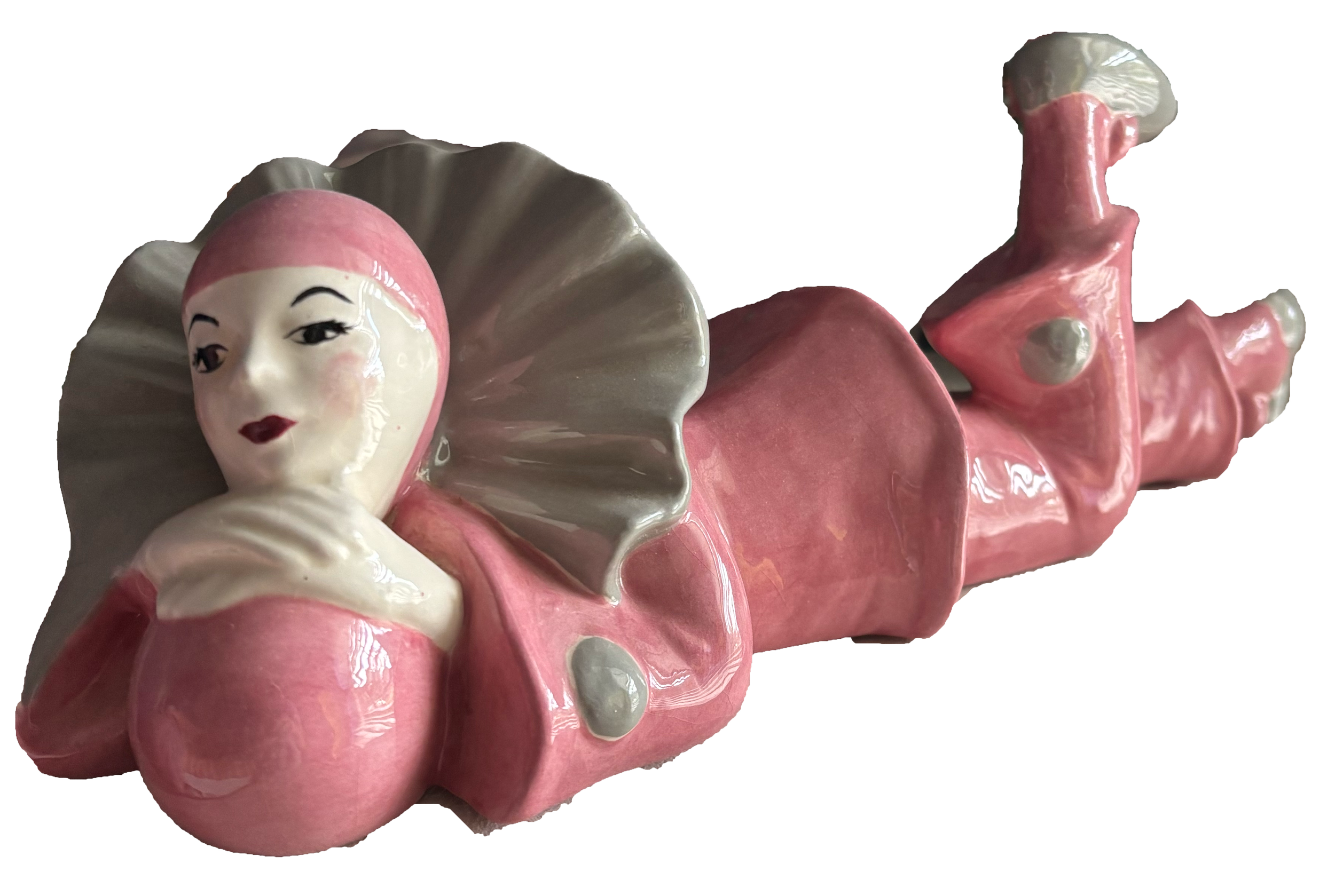 A decorative porcelain figurine of a clown with a female face, pink hat, ruffled collar, and pink clothing lying on its side.