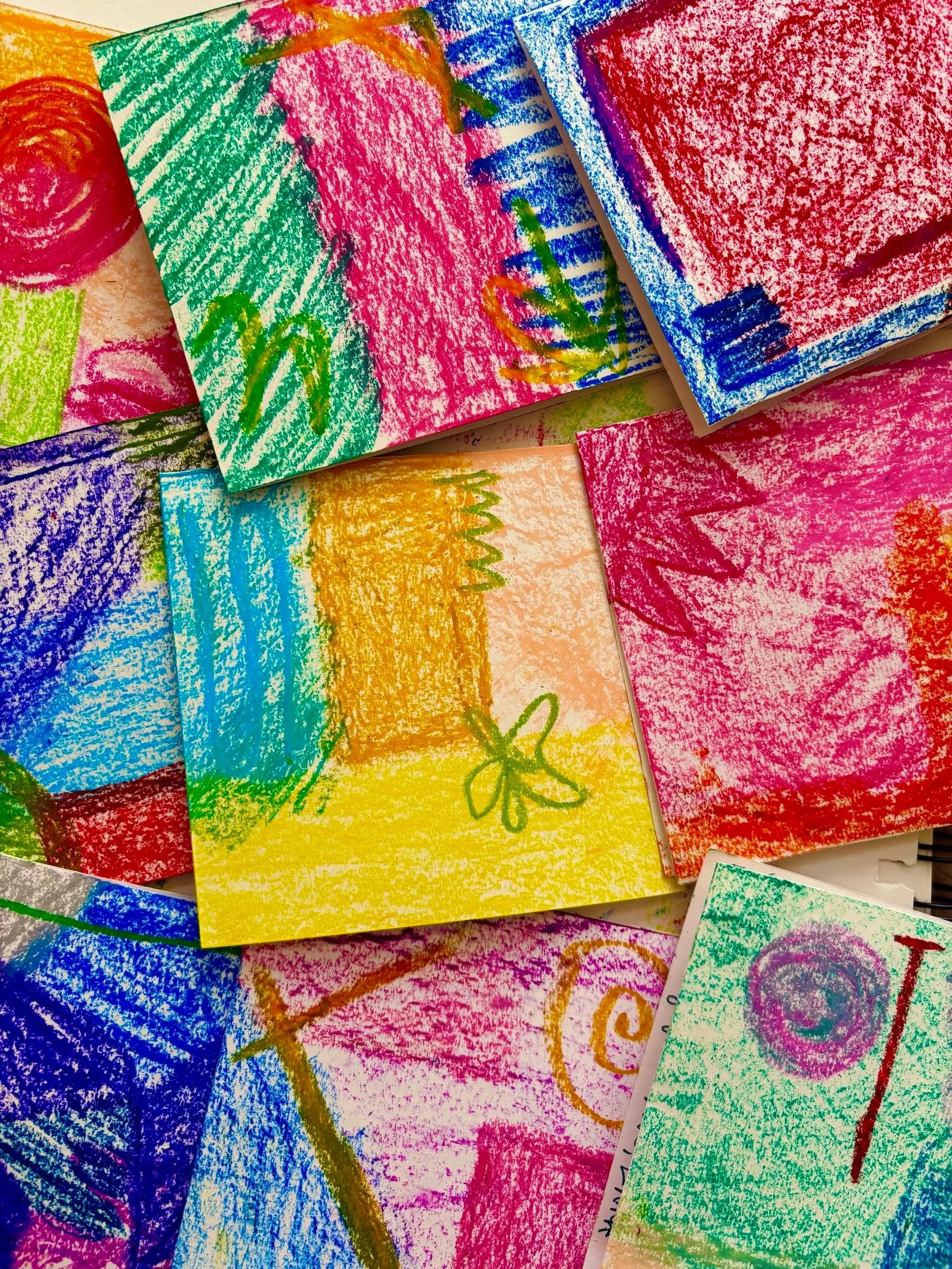 Colorful oil pastel drawings on small pieces of paper, featuring abstract shapes, lines, and some whimsical designs.