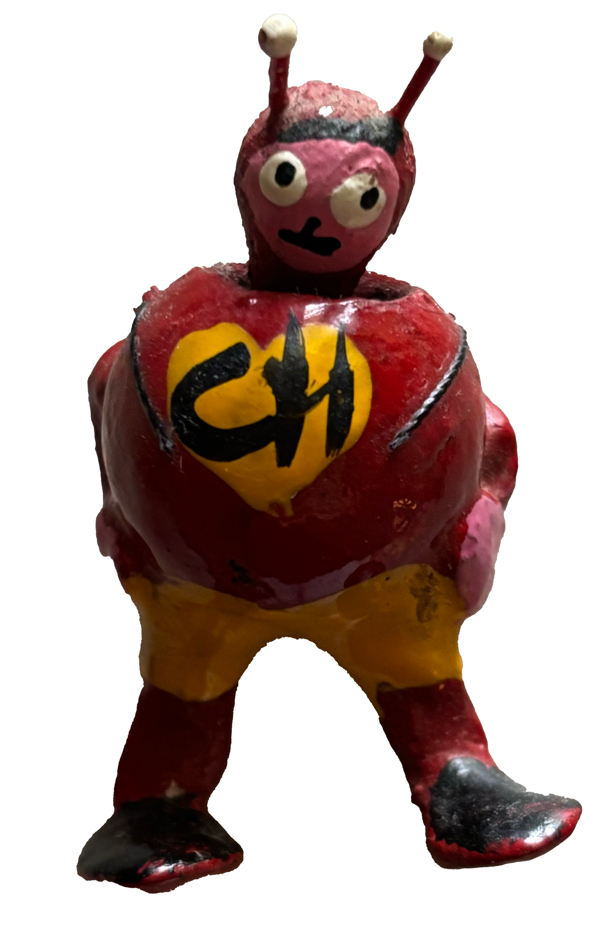 A colorful sculpture resembling a humanoid character with a red and yellow body, pink head, large eyes, and antennae, featuring a yellow heart with black symbol on its chest.