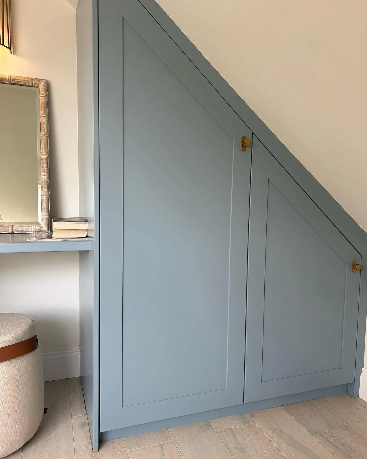 A blue closet with a sloped top, built into an attic or under a staircase, with two brass knobs.