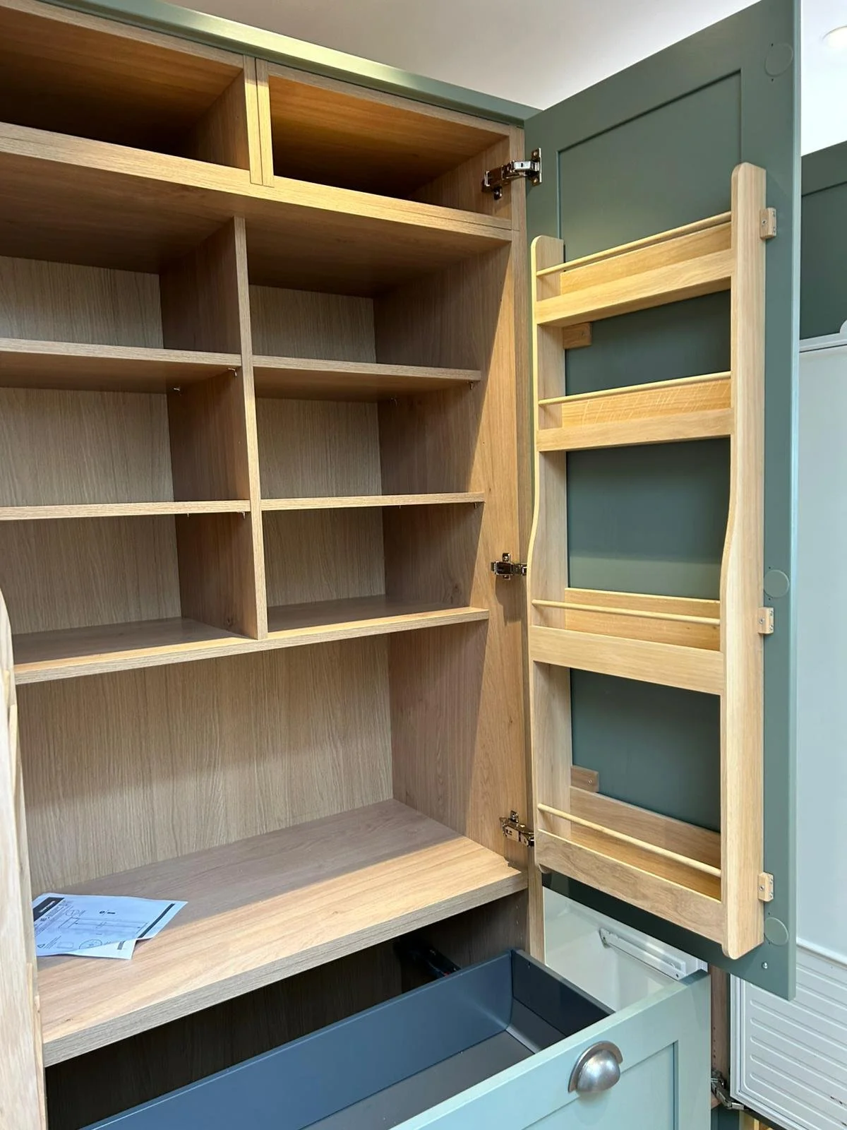 Open kitchen cabinet with empty shelves and a folding wooden tray attached to the inside of the door.