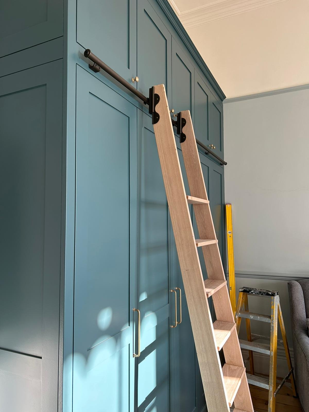A blue built-in tall cabinet in a room with a ladder and a yellow level leaning against the wall.