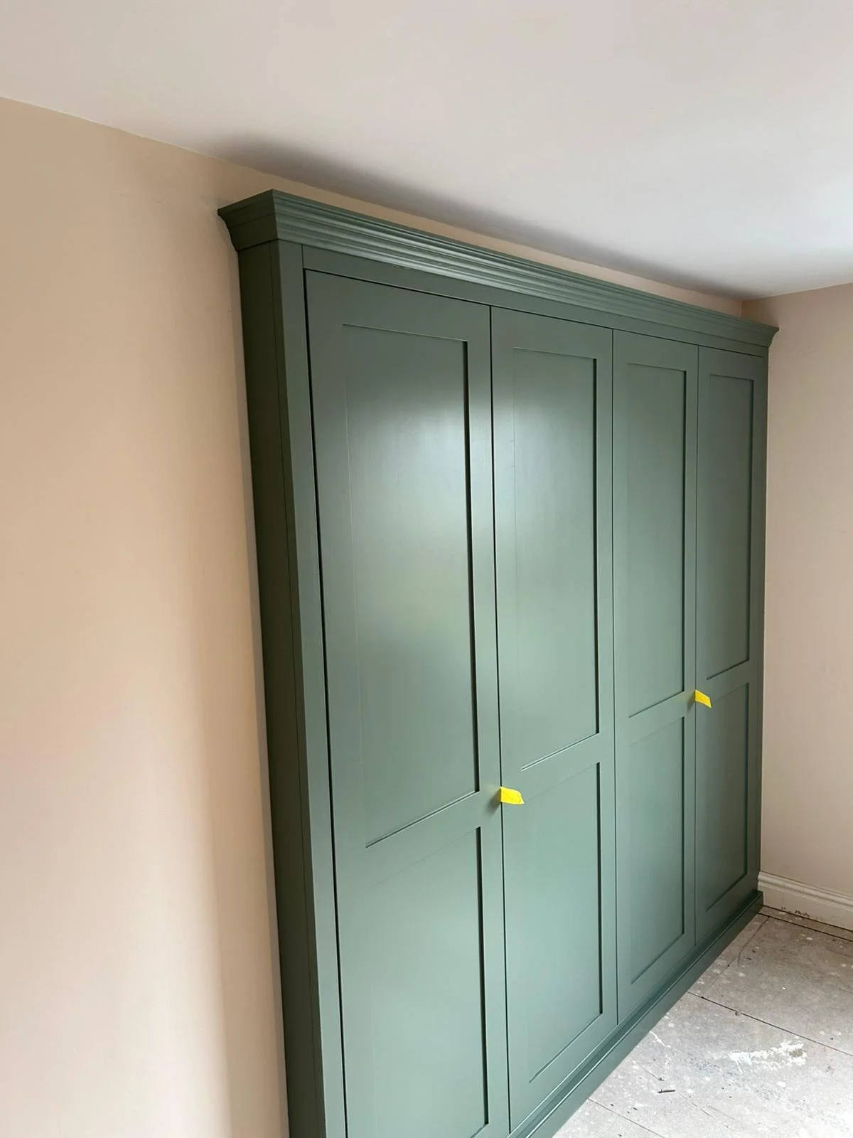 Green wardrobe with paneled doors in a room with beige walls and a concrete floor.
