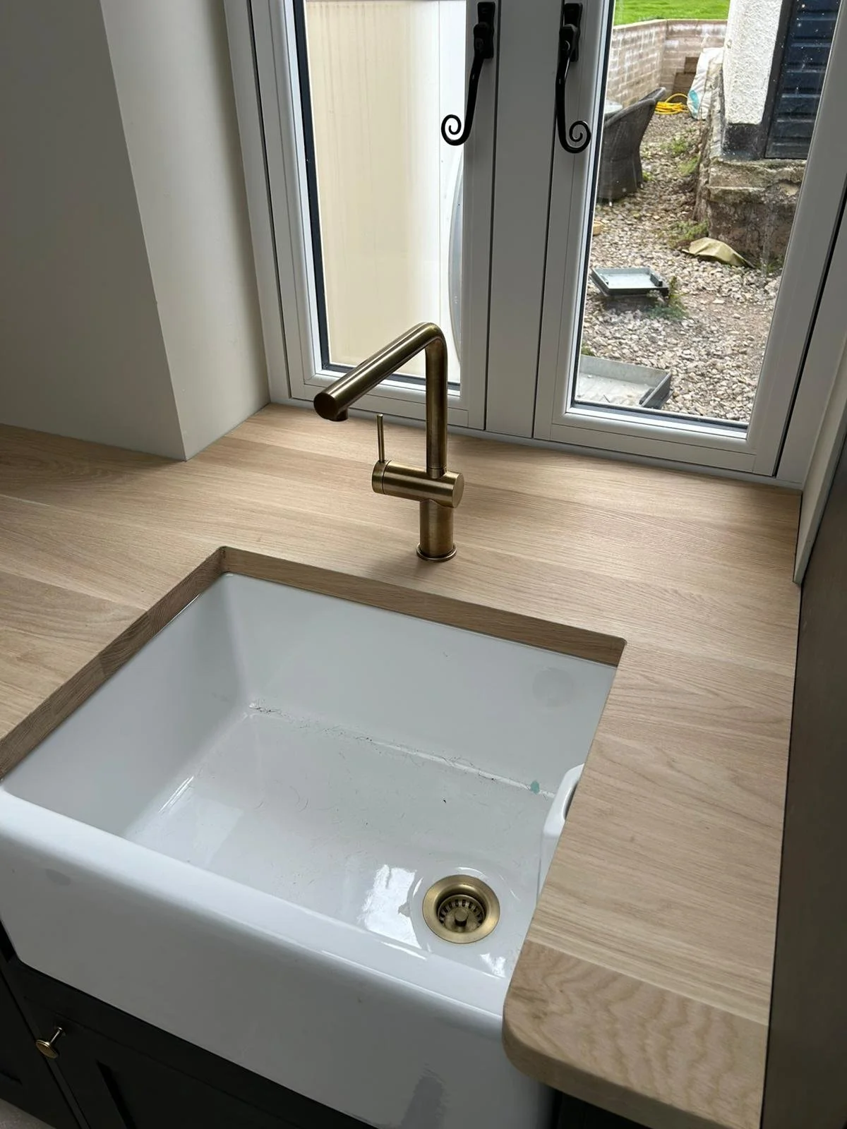 A kitchen sink with a brass faucet set into a wooden countertop near a window overlooking a garden.