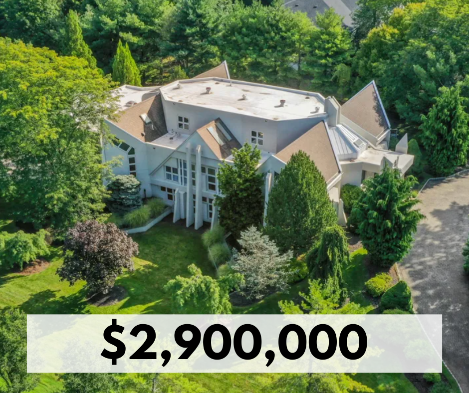 A large white mansion surrounded by lush green trees and landscaping. The house has multiple roof sections and large windows, with a driveway visible on the right side. Price is listed as $2,900,000.