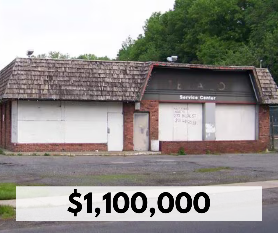 An abandoned building with boarded windows and a faded sign reading 'Service Center.' The building has a shingled roof and brick walls. The lot is empty, and the building looks unused. The text overlay shows a price of $1,100,000.
