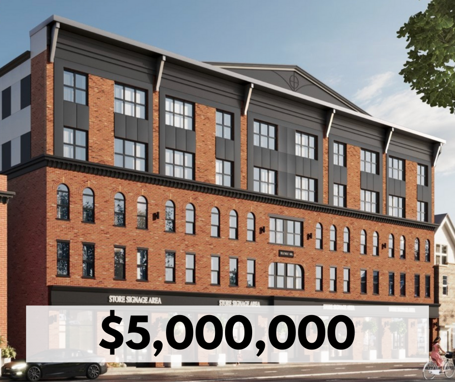 A four-story brick and gray modern commercial building with multiple windows, including arched windows on the first floor, and store signage areas on the ground floor, situated on a street with cars and a cyclist.