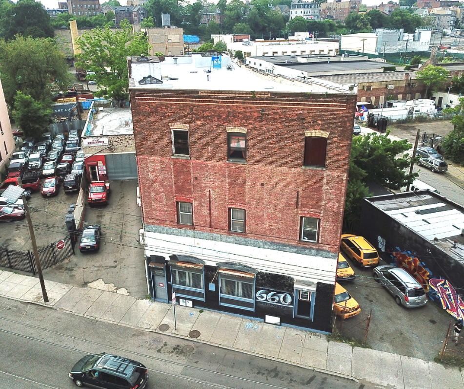 A four-story brick building with a business named 660 on the ground floor, situated on a city street with parked cars and surrounding structures.