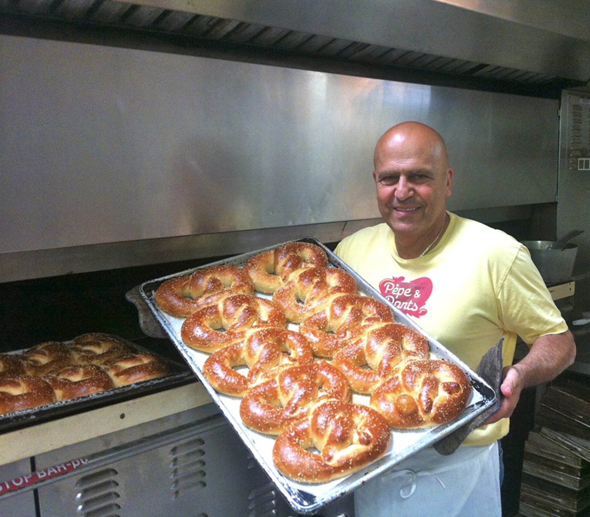 A man holding a tray filled with freshly baked pretzels in a commercial kitchen.