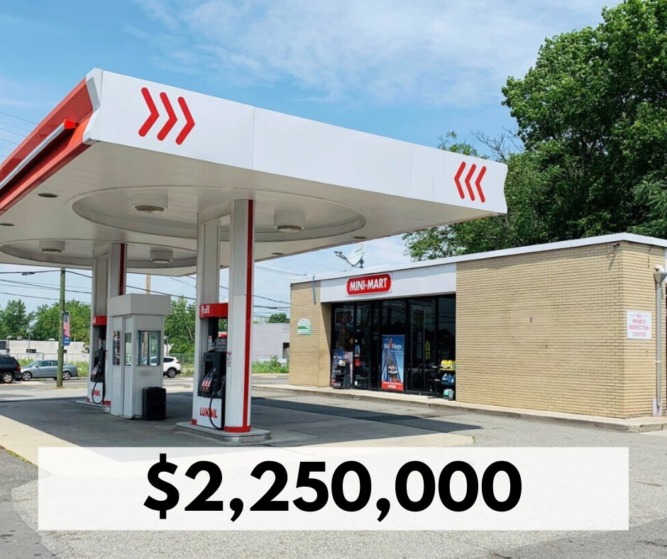 A gas station with a canopy and pumps in front of a convenience store, with trees and a blue sky in the background.