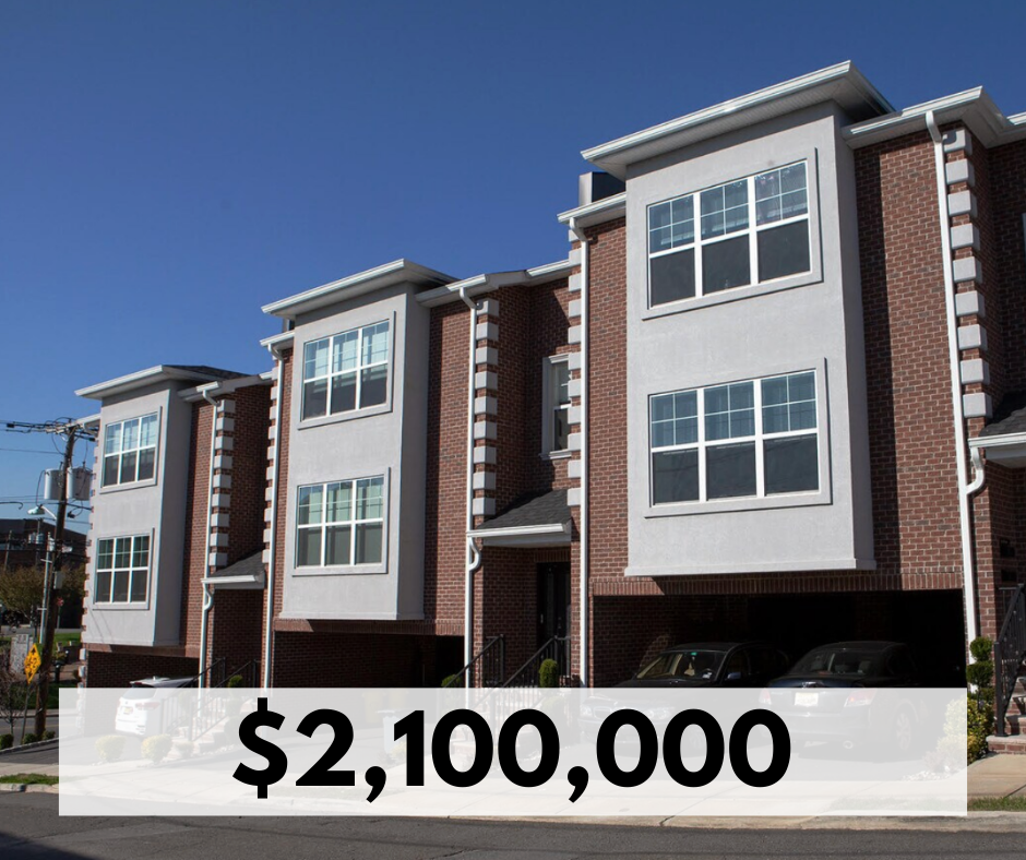 A row of modern four-story townhouses with brick and white exterior, large windows, and small front porches, under a clear blue sky.