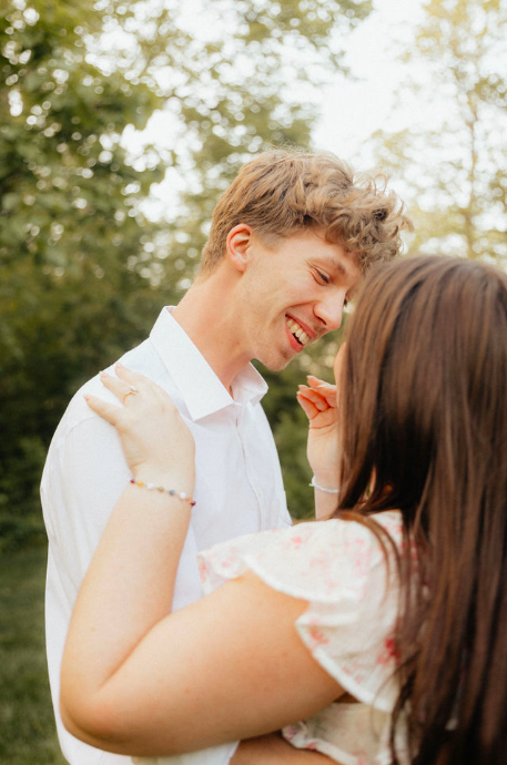 A young couple smiling and embracing outdoors among trees on a sunny day