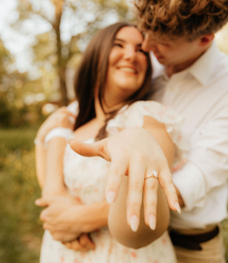 Couple embracing outdoors, the woman showing off an engagement ring on her finger