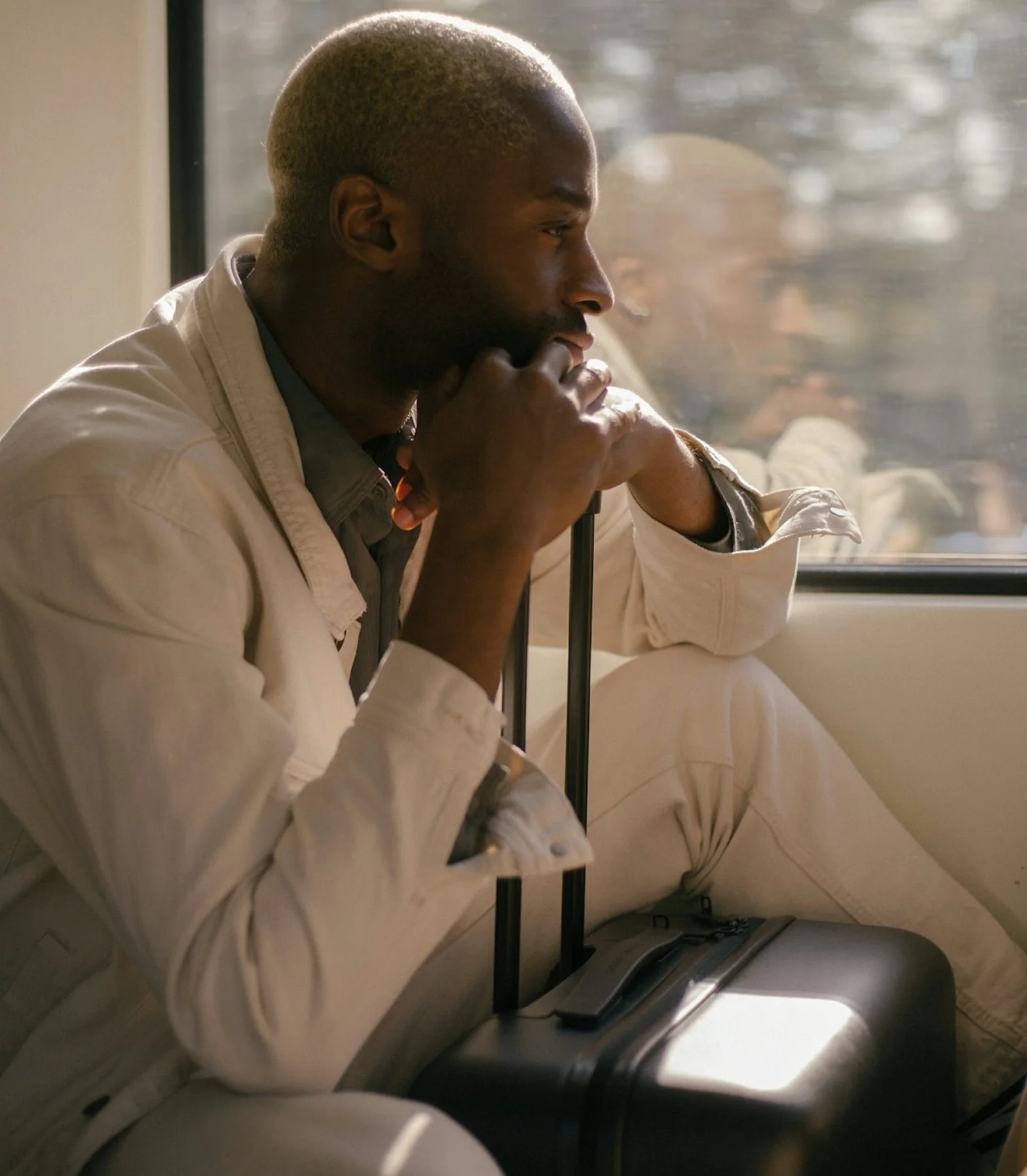 Man on a train resting his head on his suitcase handle and staring out the window. Light reflection in the glass.