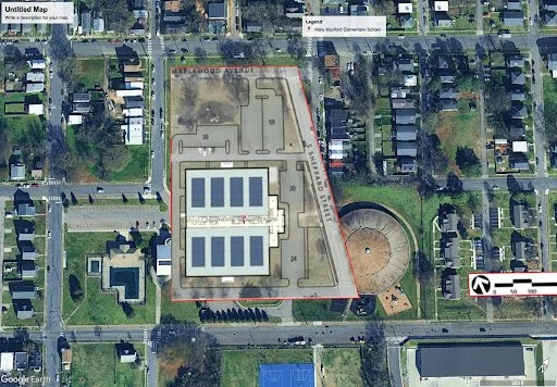 Aerial view of Mary McLeod Bethune Elementary School with solar panels on the roof, a nearby circular playground, tennis courts, and surrounding residential area.