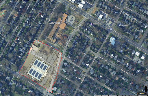 Aerial view of a neighborhood with a building complex, parking lot, and surrounding residential homes and streets.