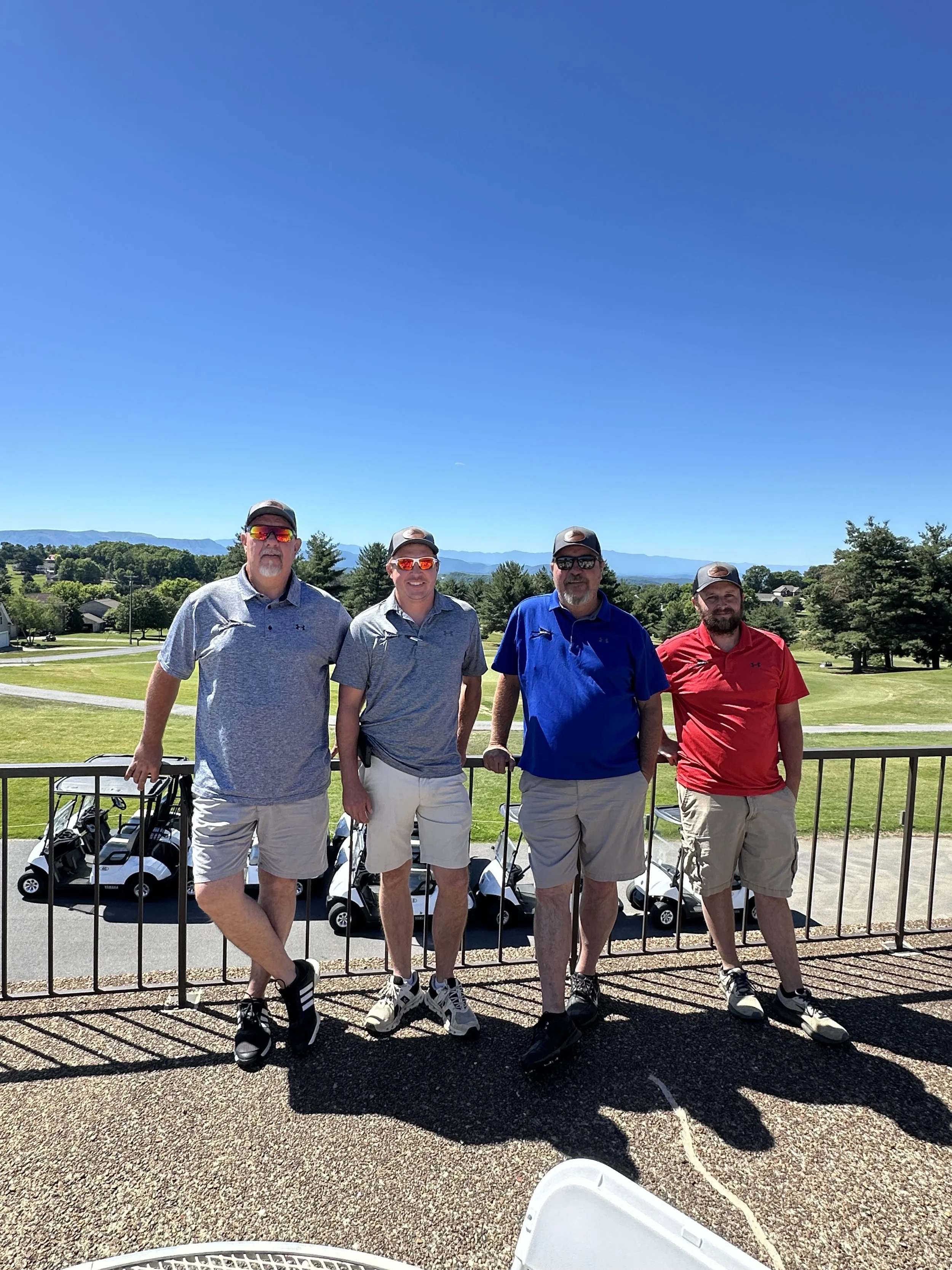 Four men standing in front of a golf course looking towards the camera. Precision Structures, Inc at the Jefferson County Chamber of Commerce Golf Tournament.
