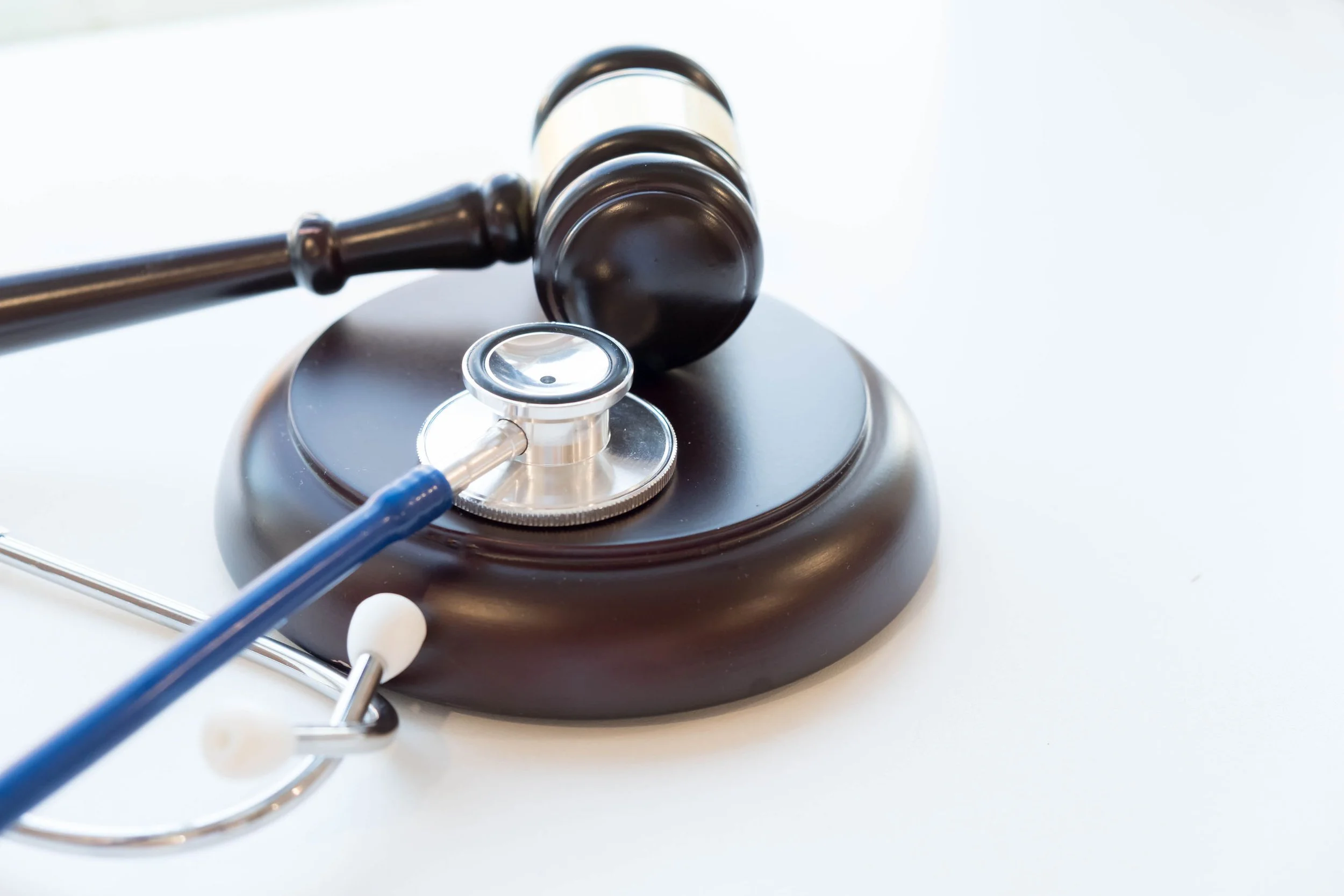 A gavel resting on a sound block, a stethoscope, and a hearing aid on a white surface.