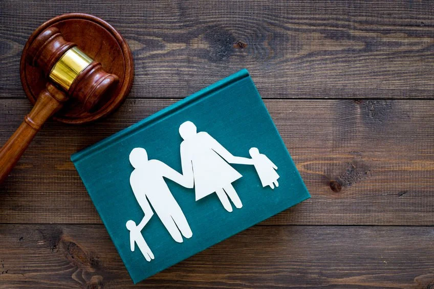 A wooden gavel beside a teal book with paper cutouts of a family holding hands, on a wooden surface.