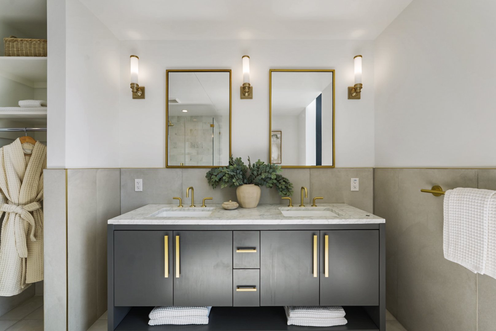 Modern bathroom with dual sinks, gold fixtures, mirrors, a vase with greenery, and a vanity cabinet with towels underneath.