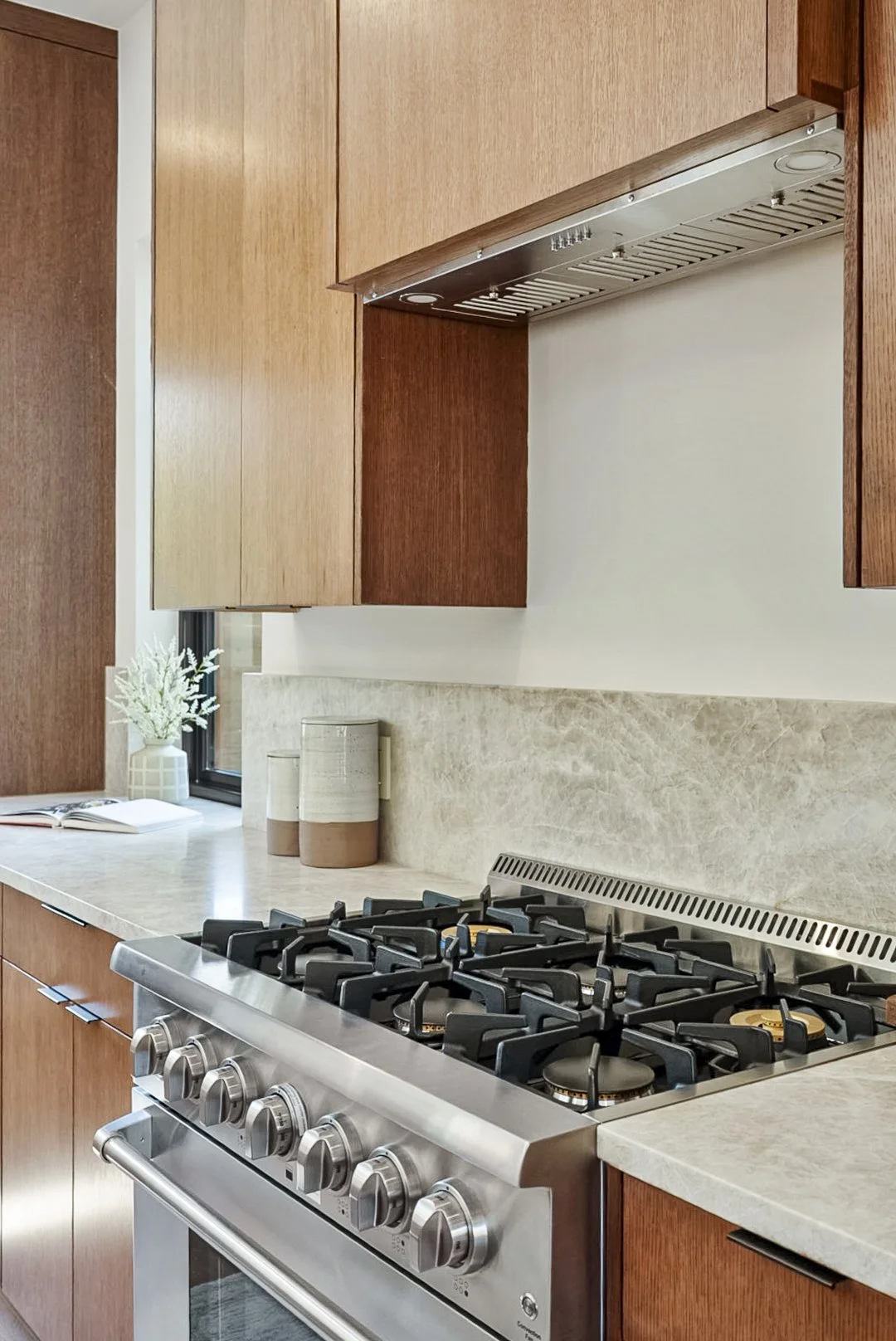Kitchen with wooden cabinets, a marble countertop, a gas stove, a small potted plant, a book, and decorative vases.