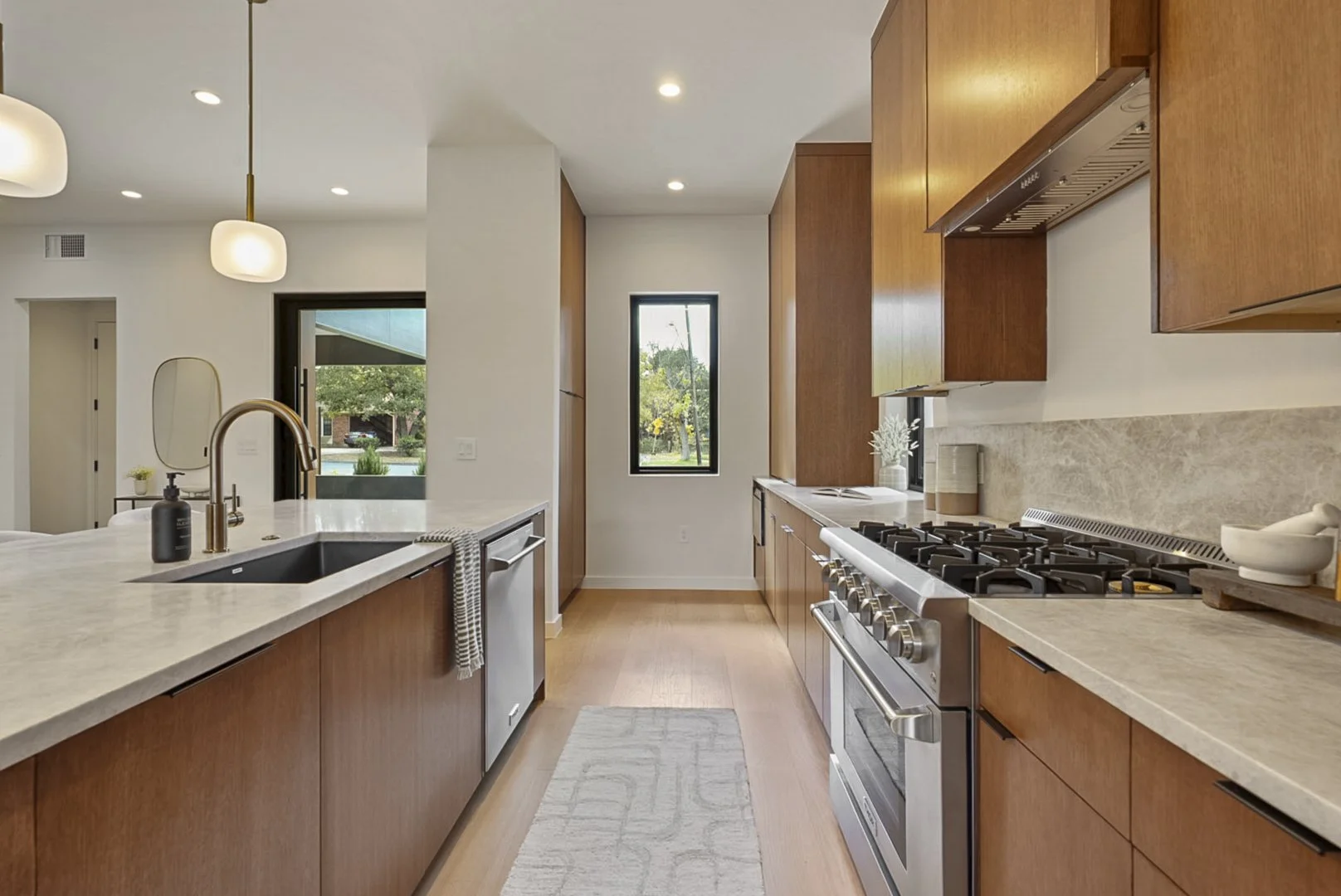 Modern kitchen with wooden cabinets, stainless steel stove, light-colored countertops, and a small window with greenery outside