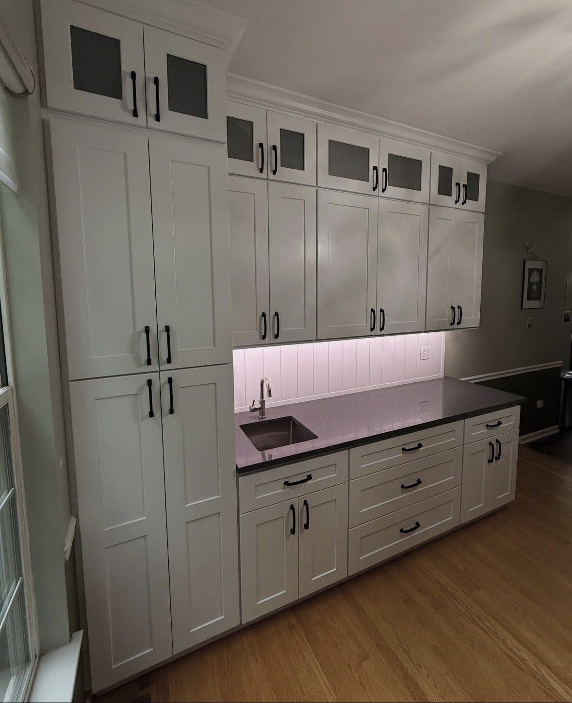 Kitchen with white cabinets, black handles, a dark countertop, a small sink, and a wooden floor.