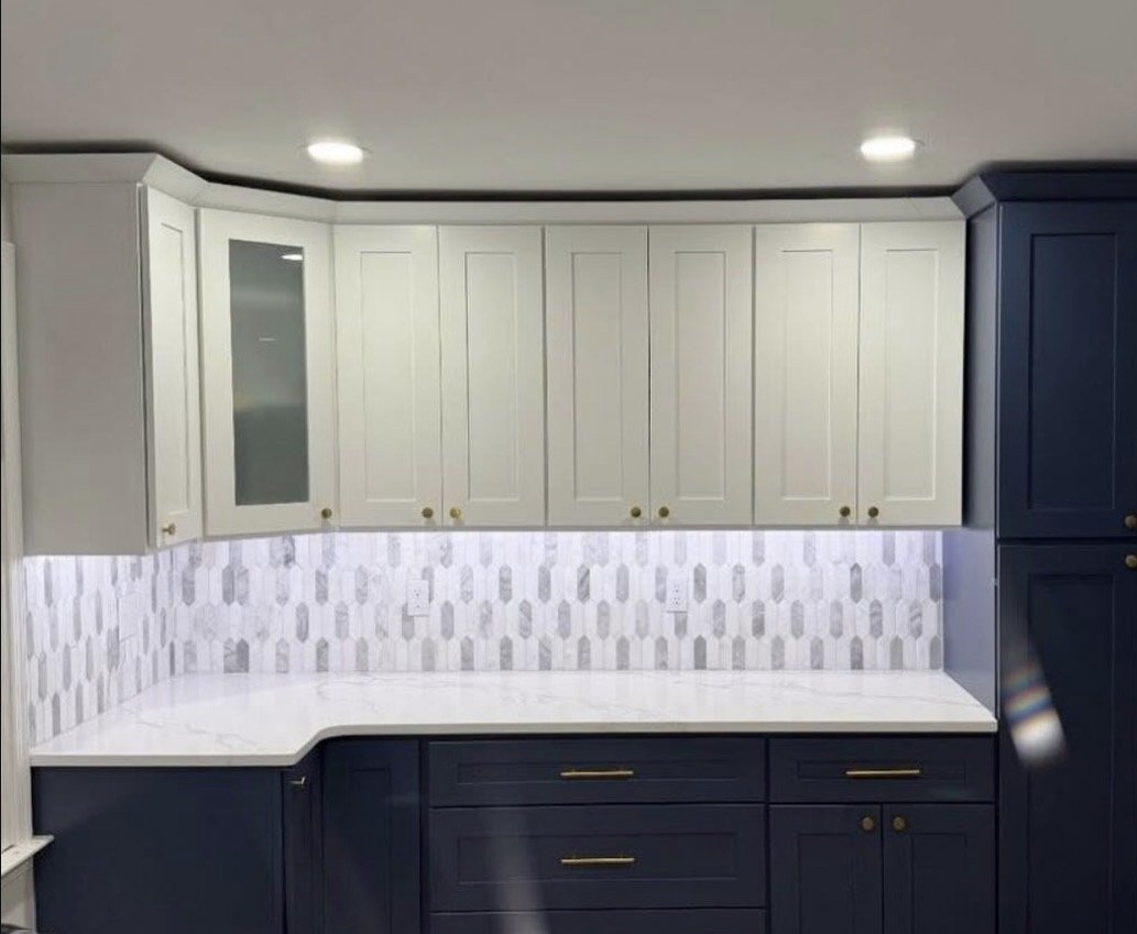 Kitchen cabinets with white upper cabinets, navy lower cabinets, a white marble countertop, and a white tile backsplash with a geometric pattern.