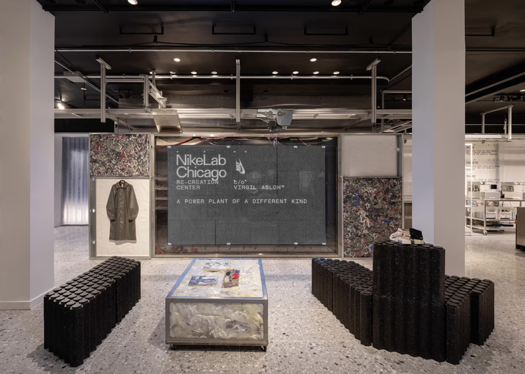 Display booth at NikeLab Chicago Re-Creation Center featuring magazines, a briefcase with artwork, and promotional materials on a table with a metallic and textured design. Background has a mural with flowers.