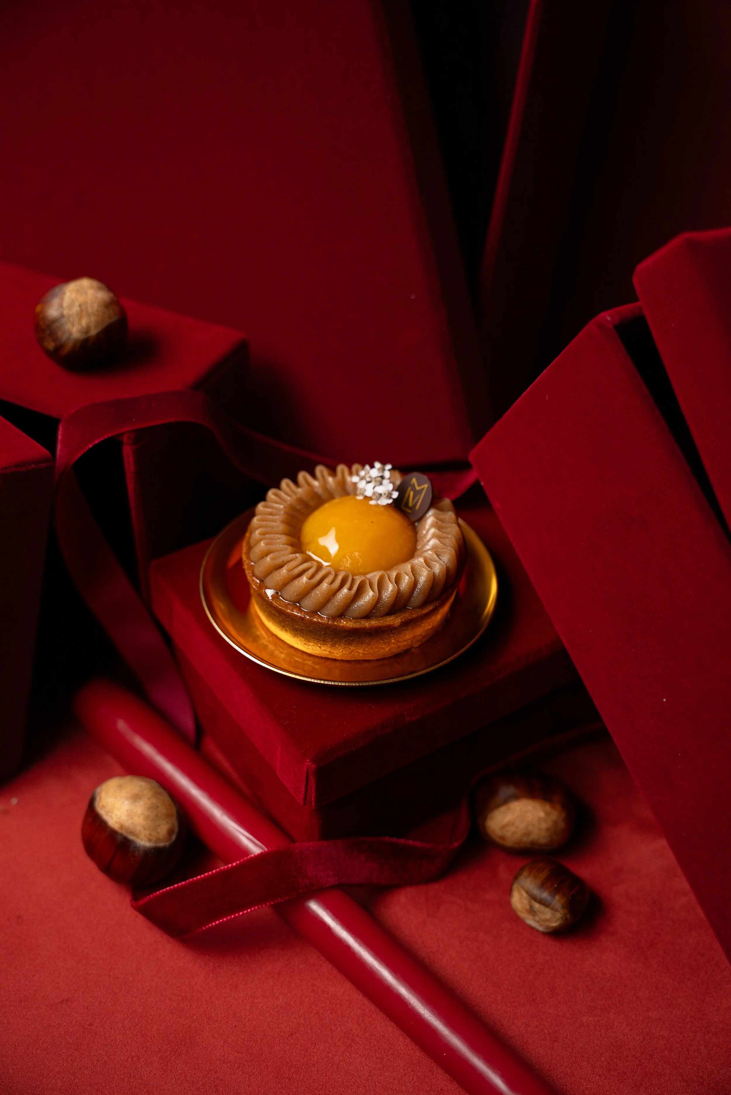 Un dessert élégant avec une texture onctueuse et un topping brillant, présenté dans une boîte rouge avec ruban en satin.