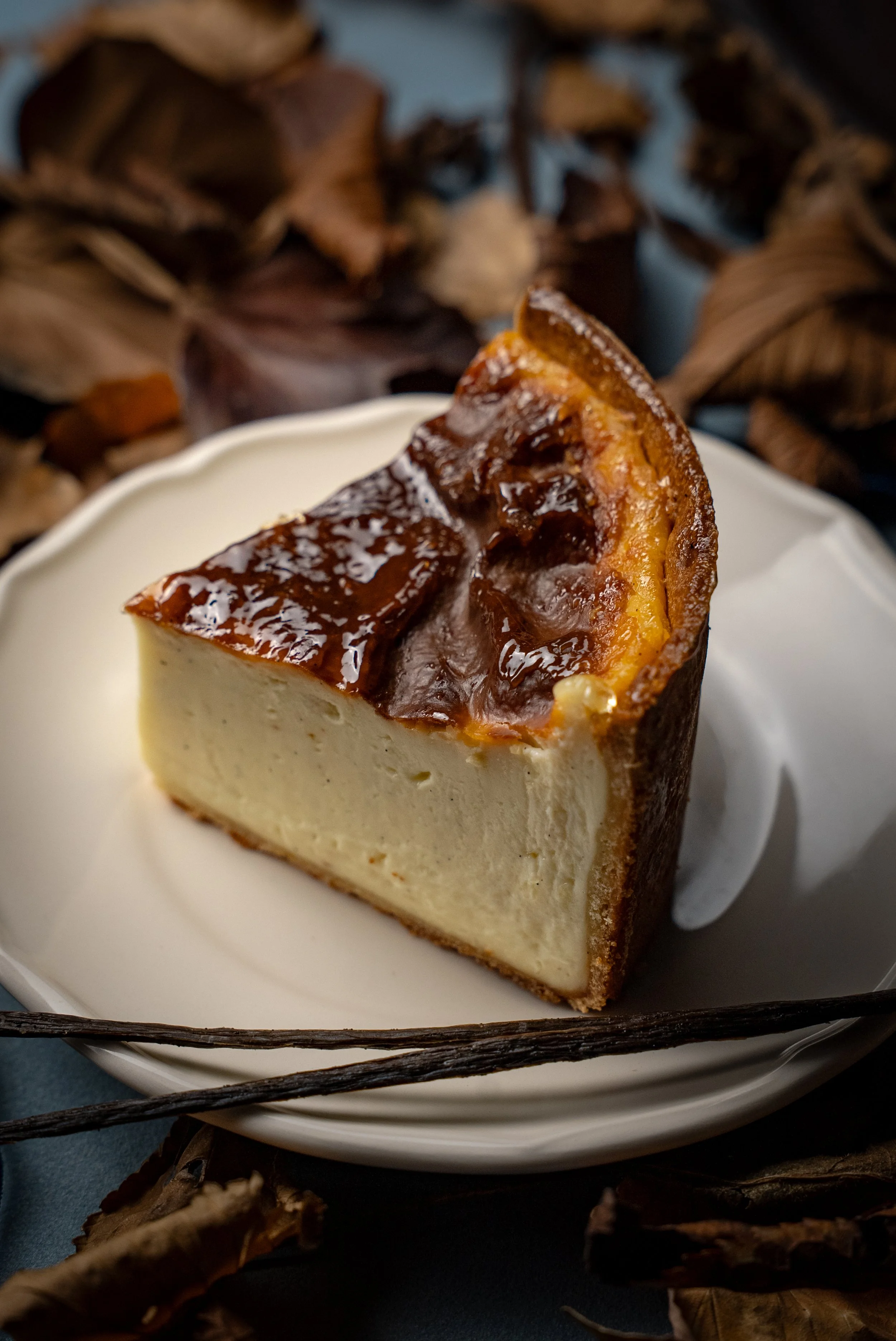 Part de cheesecake avec une garniture caramelisée sur le dessus, servie dans une assiette blanche, avec des feuilles d'automne en arrière-plan.