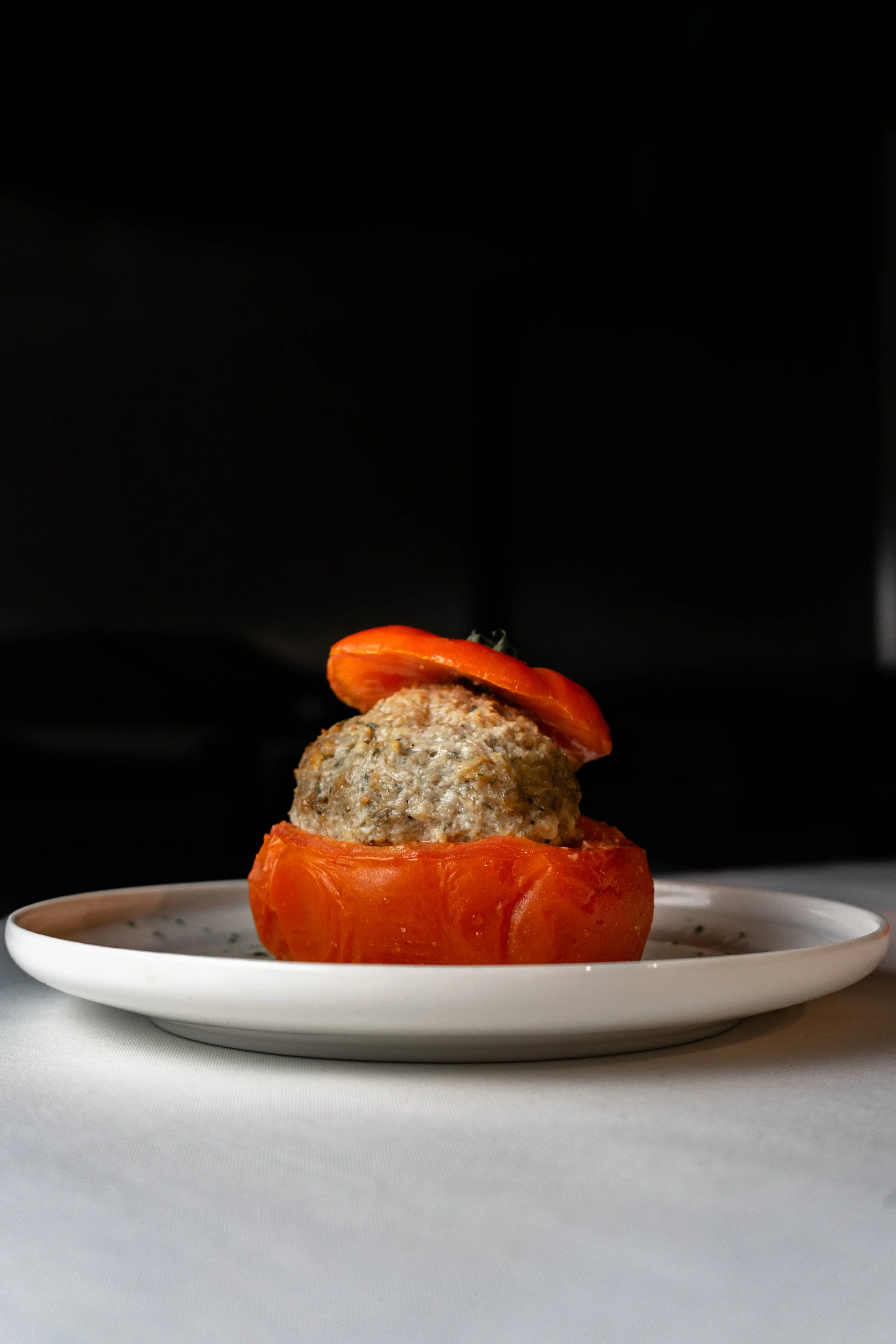 Un plat avec une tomate rouge coupée, contenant une boule de farce, avec une tranche de tomate sur le dessus, sur une assiette blanche.