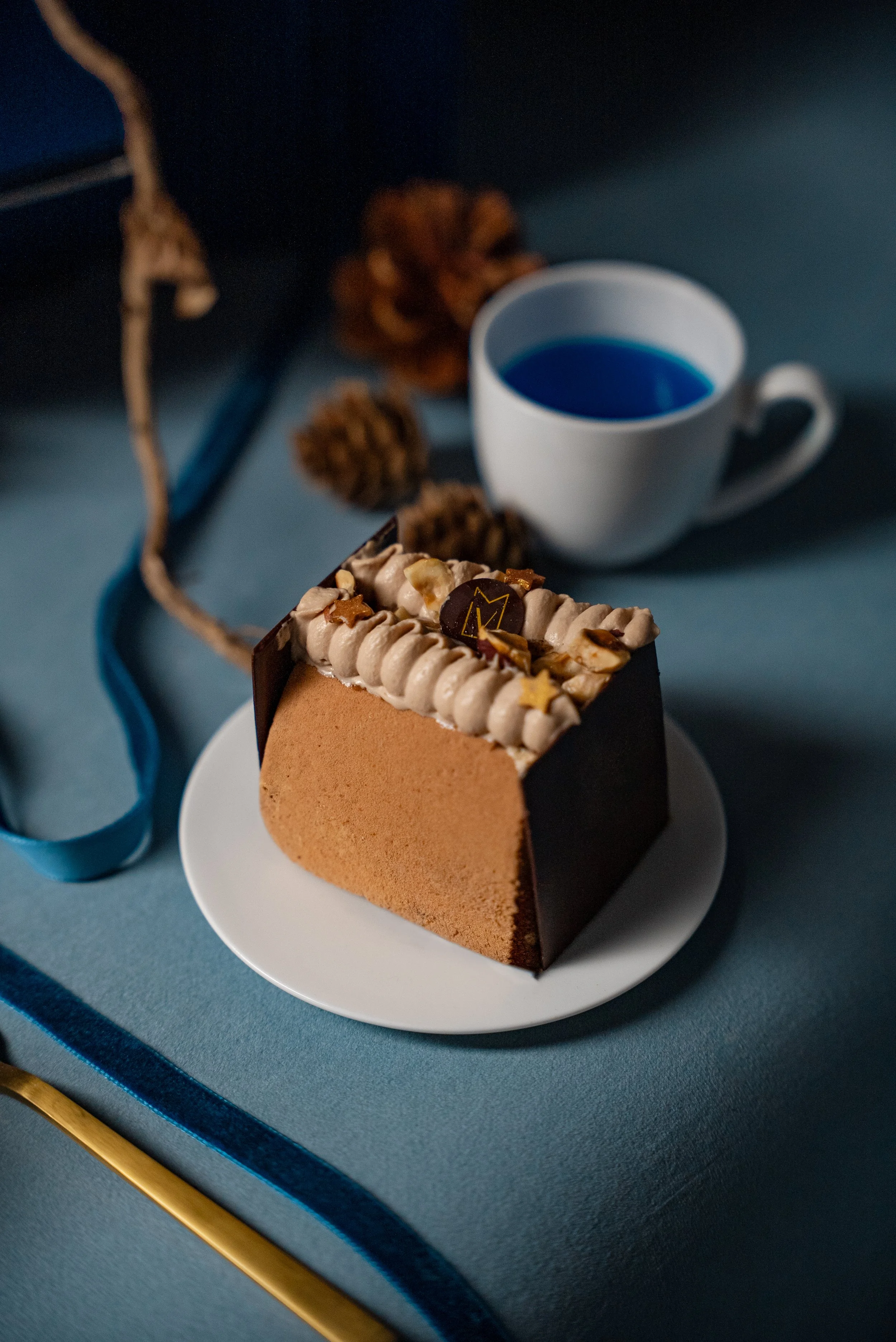 Gâteau au chocolat avec décorations en crème et étoiles en sucre, accompagné d'une tasse de boisson bleue sur une surface bleue.