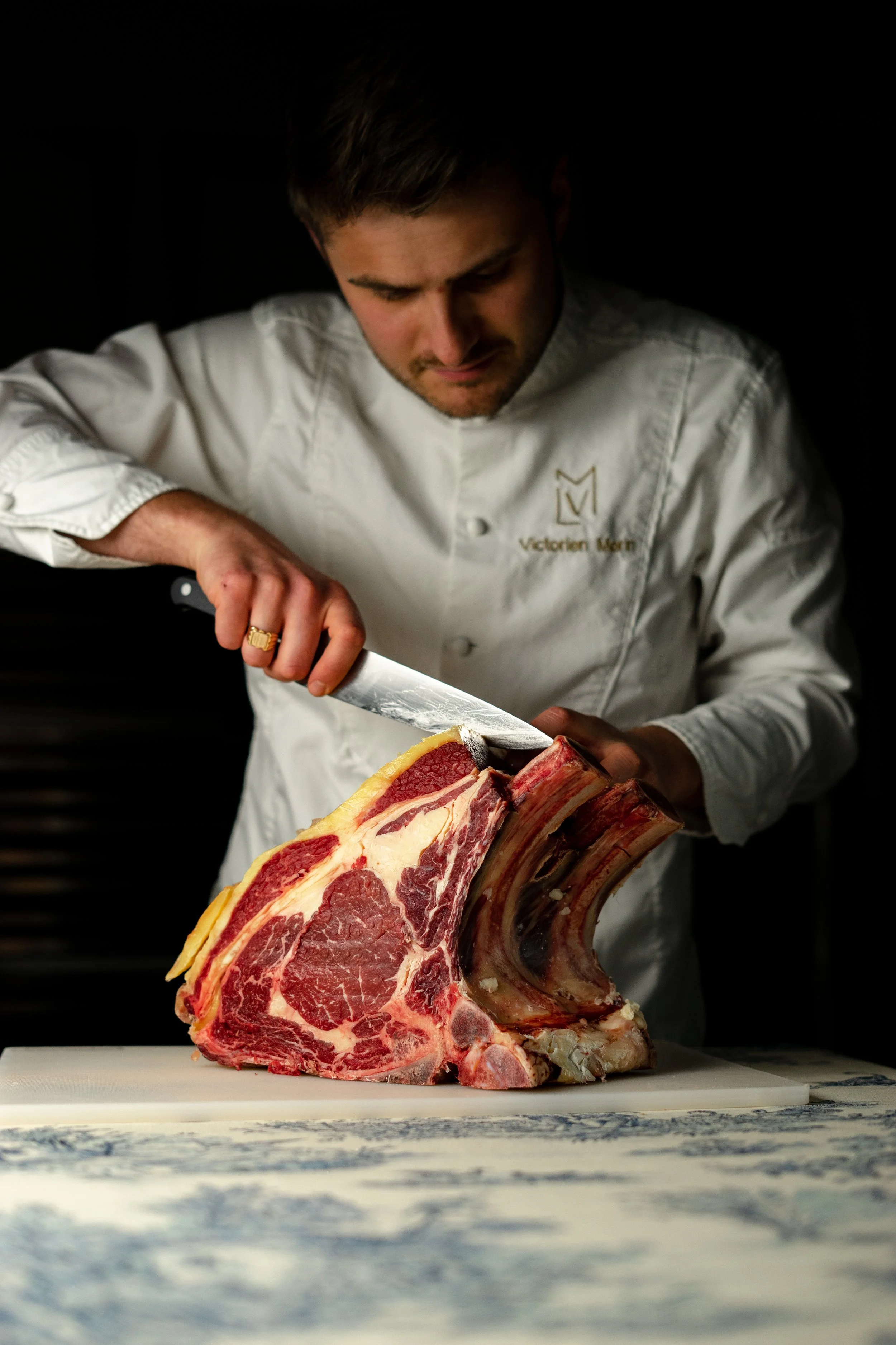 Chef en train de couper une pièce de viande de bœuf en côte de bâtre.
