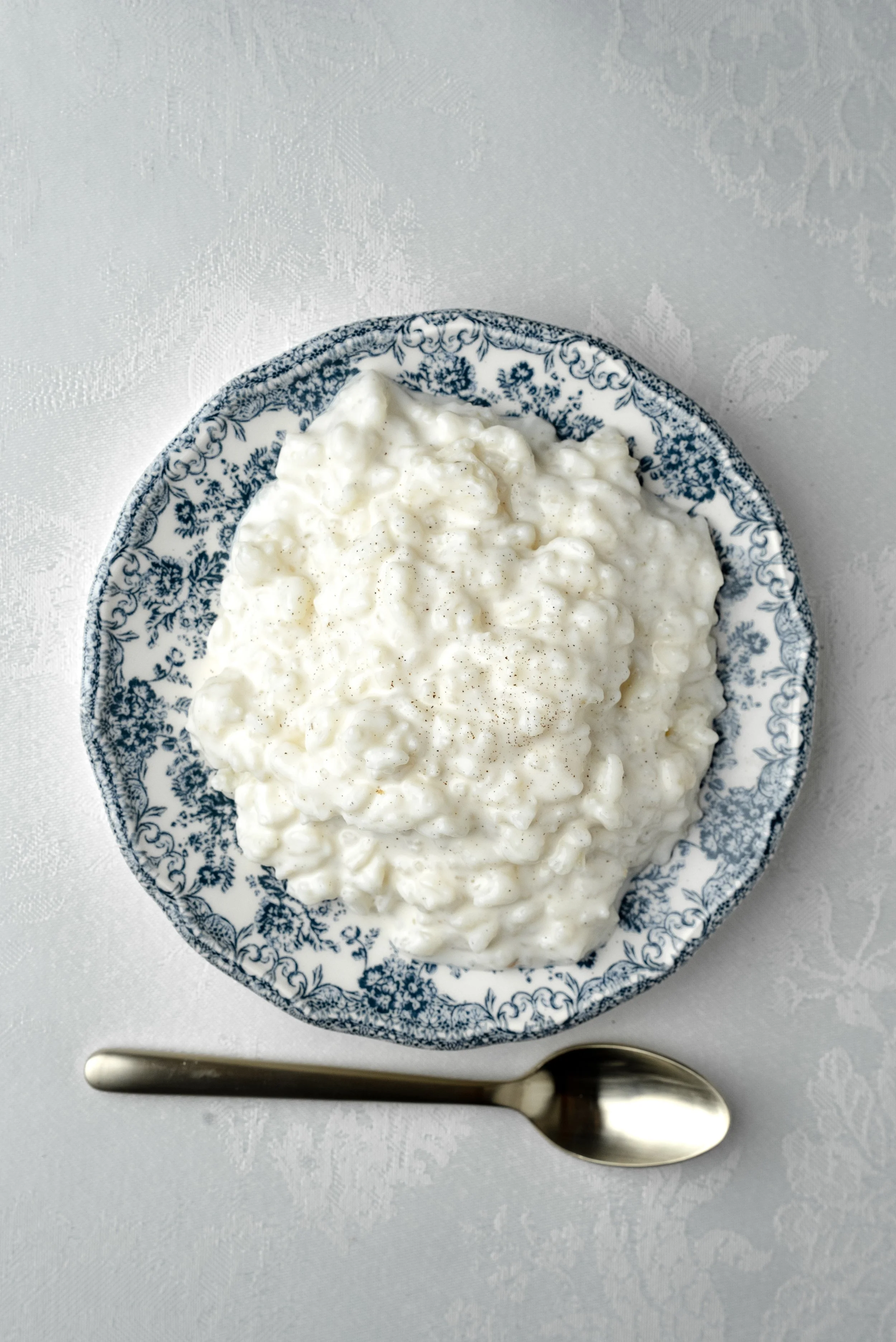 Des rillettes de porc dans une assiette à motifs bleus, accompagnées d'une cuillère en métal, sur une nappe blanche.