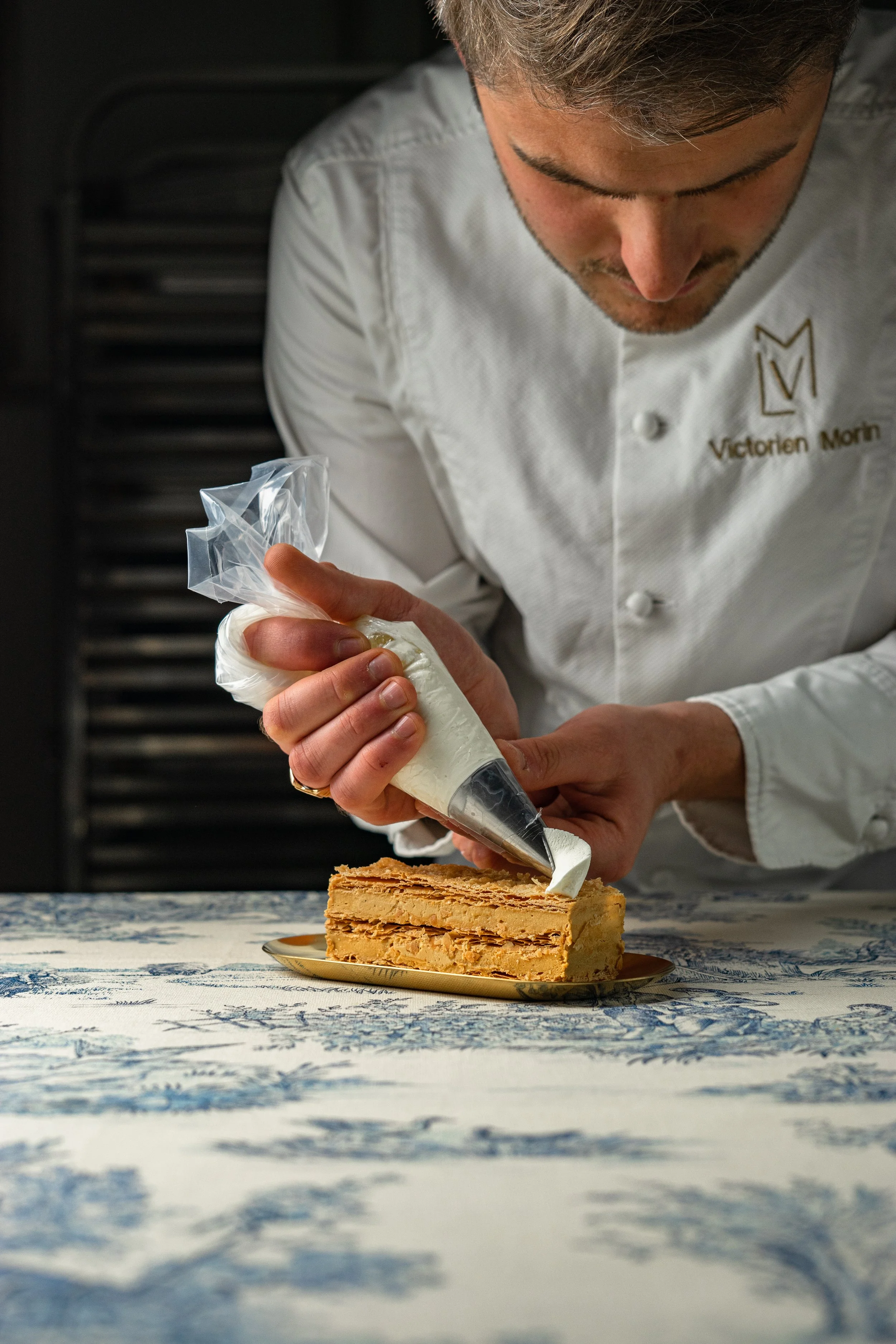 Un pâtissier décore un gâteau avec de la crème à l'aide d'une poche à douille.