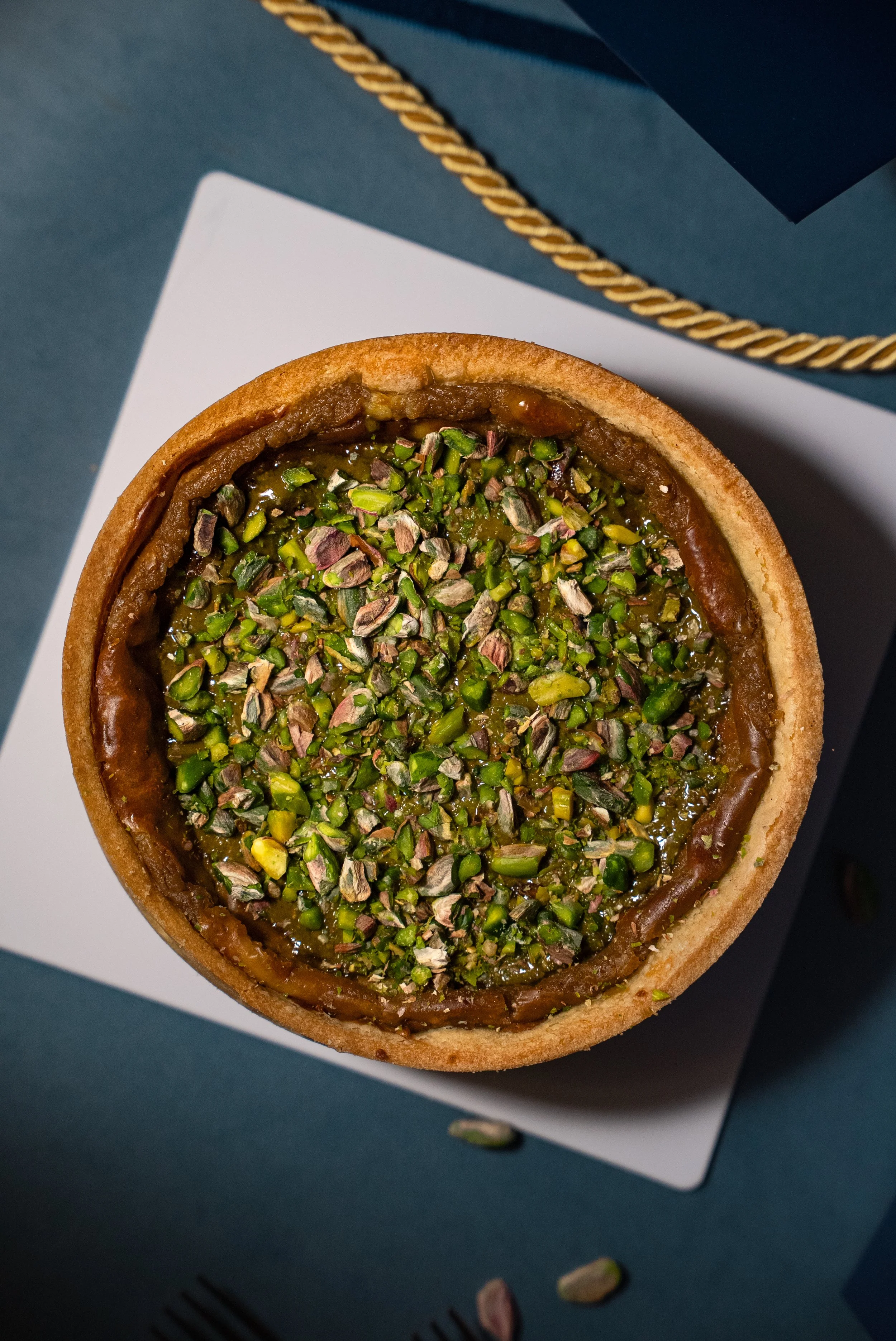 Tarte aux pistaches sur une assiette blanche, vue de dessus, avec des pistaches éparpillées autour.