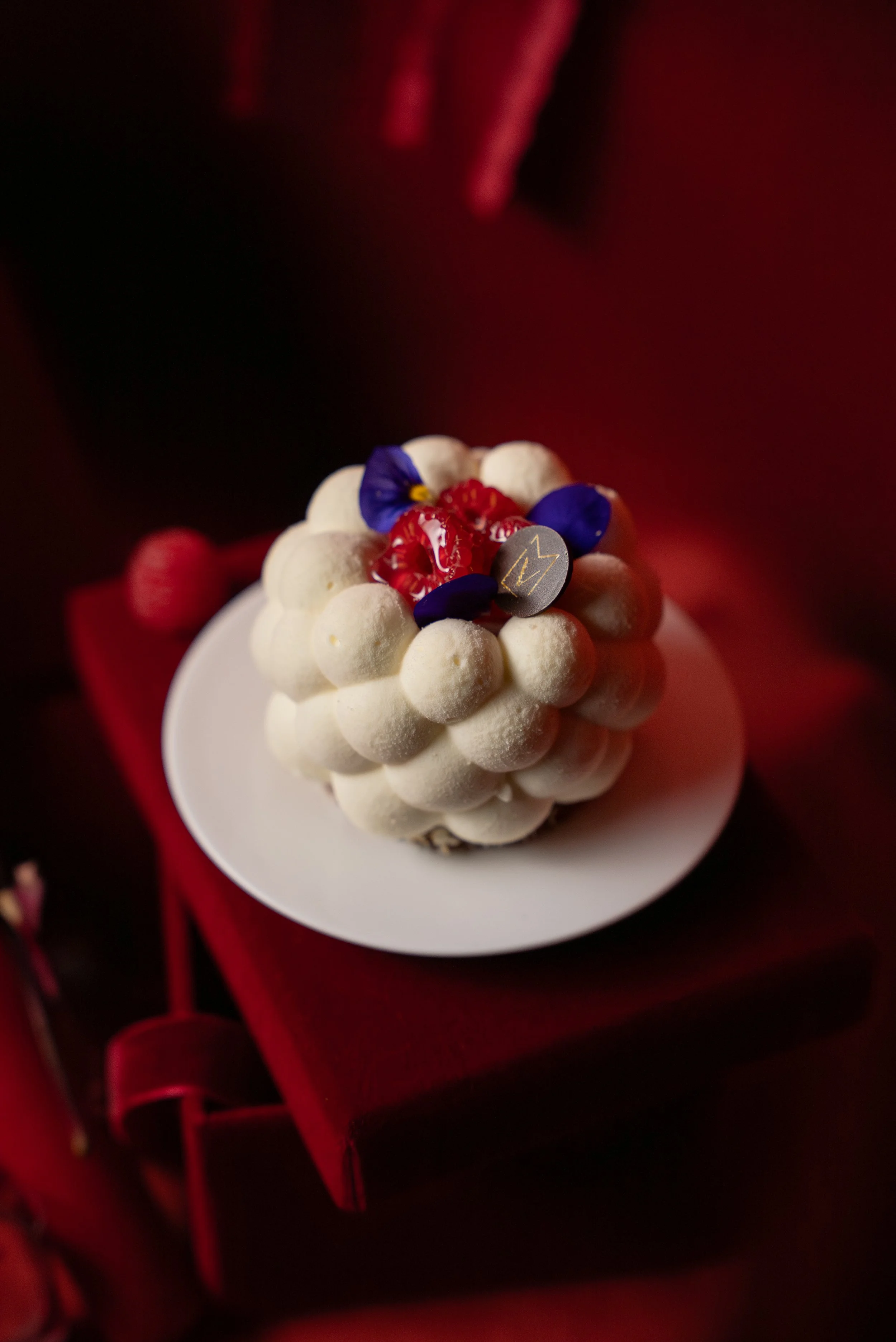 Un gâteau blanc décoré de petits biscuits, de fruits rouges et de fleurs violettes, présenté sur une assiette blanche