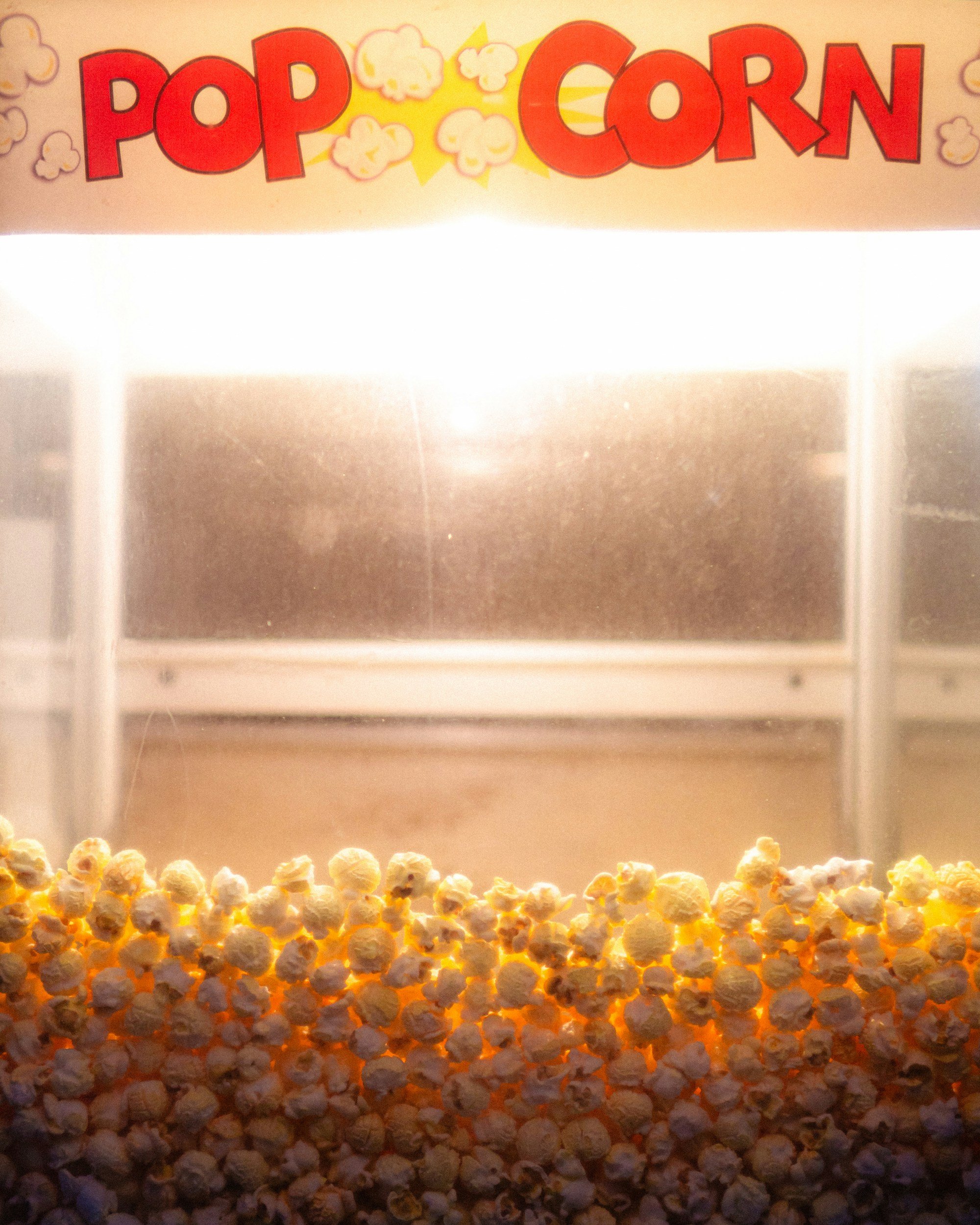 A popcorn vending machine with the word 'POP-CORN' displayed at the top, showing mostly unpopped popcorn kernels at the bottom and an illuminated empty space above for the popped popcorn.