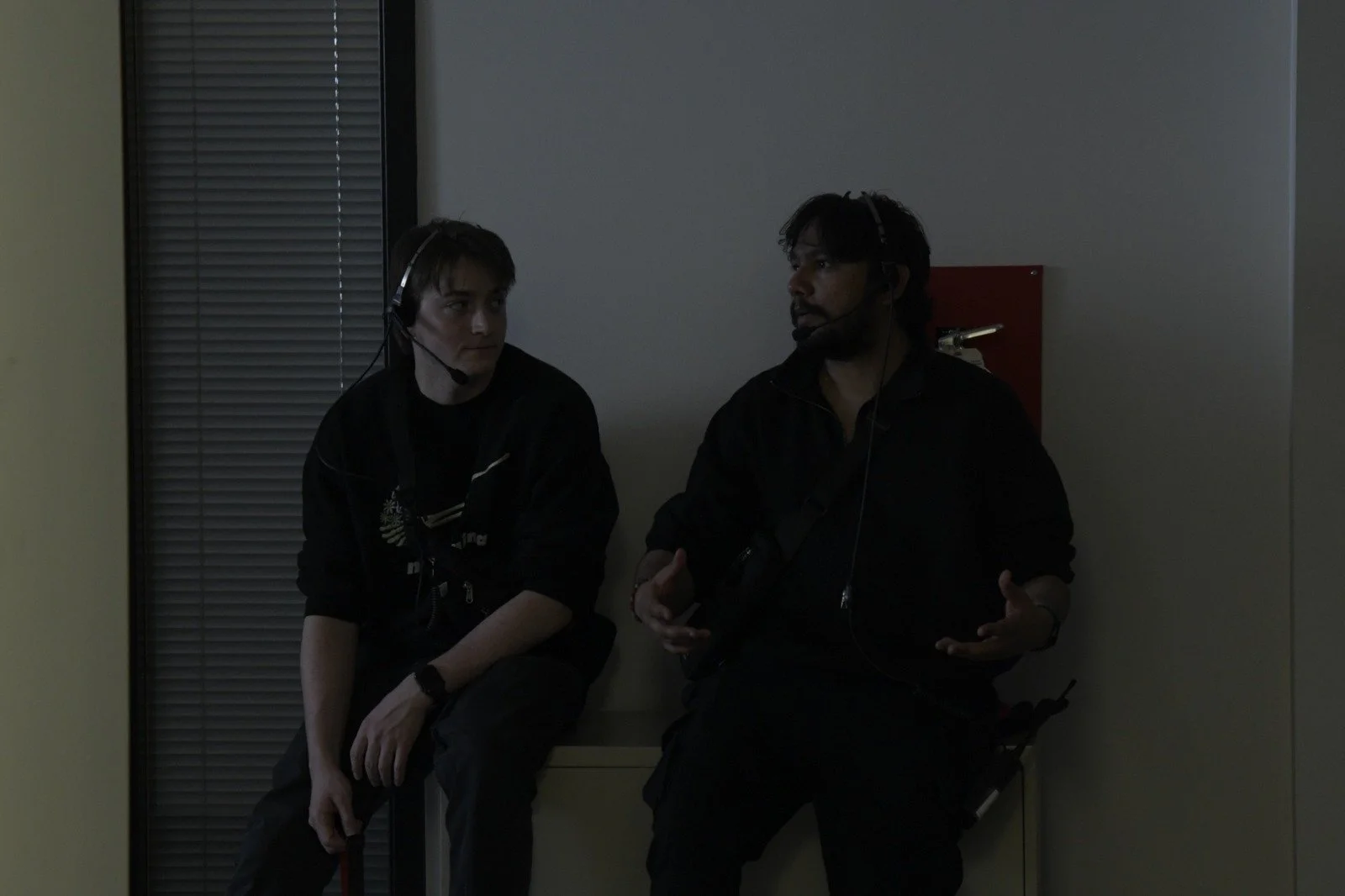 Two people including Krishna with headsets sitting in a dimly lit room, engaging in conversation.