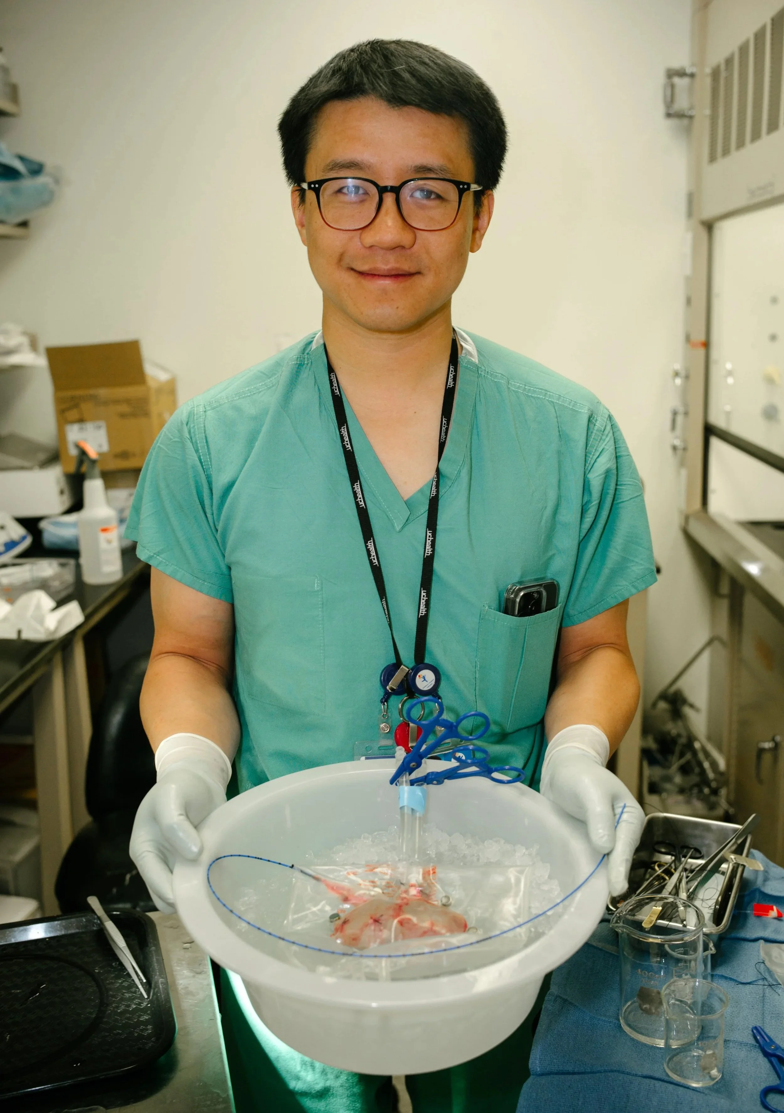 A healthcare professional in scrubs and gloves holding a tray with a dissected organ inside a clear plastic bag, in a medical setting.
