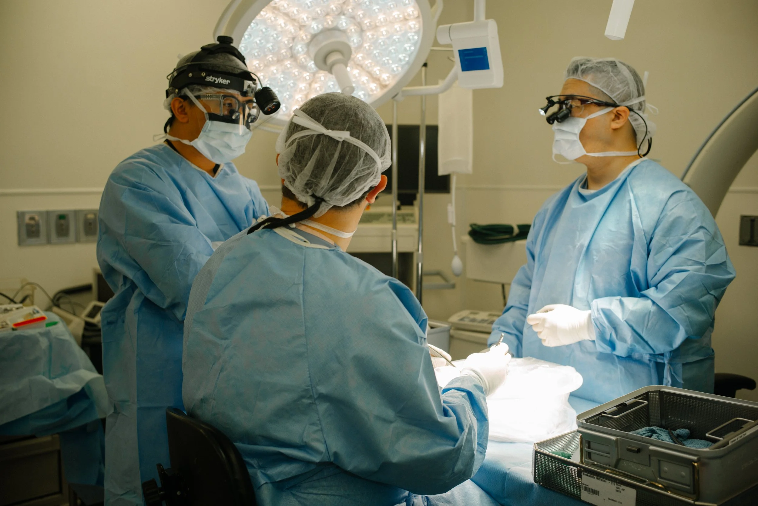 Medical team performing surgery in an operating room with surgical lights and equipment.