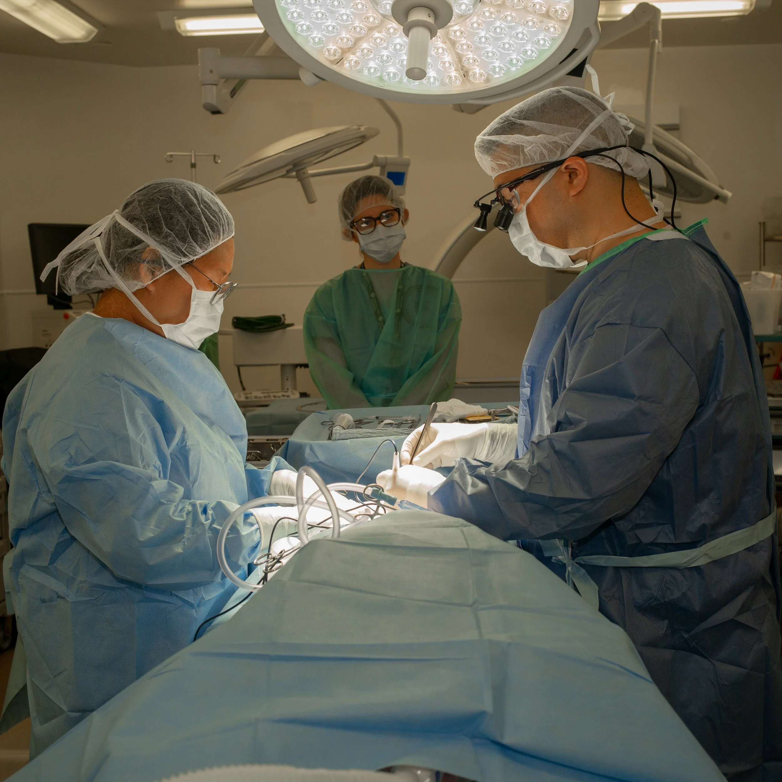 Medical team performing surgery in an operating room with surgical lights overhead.