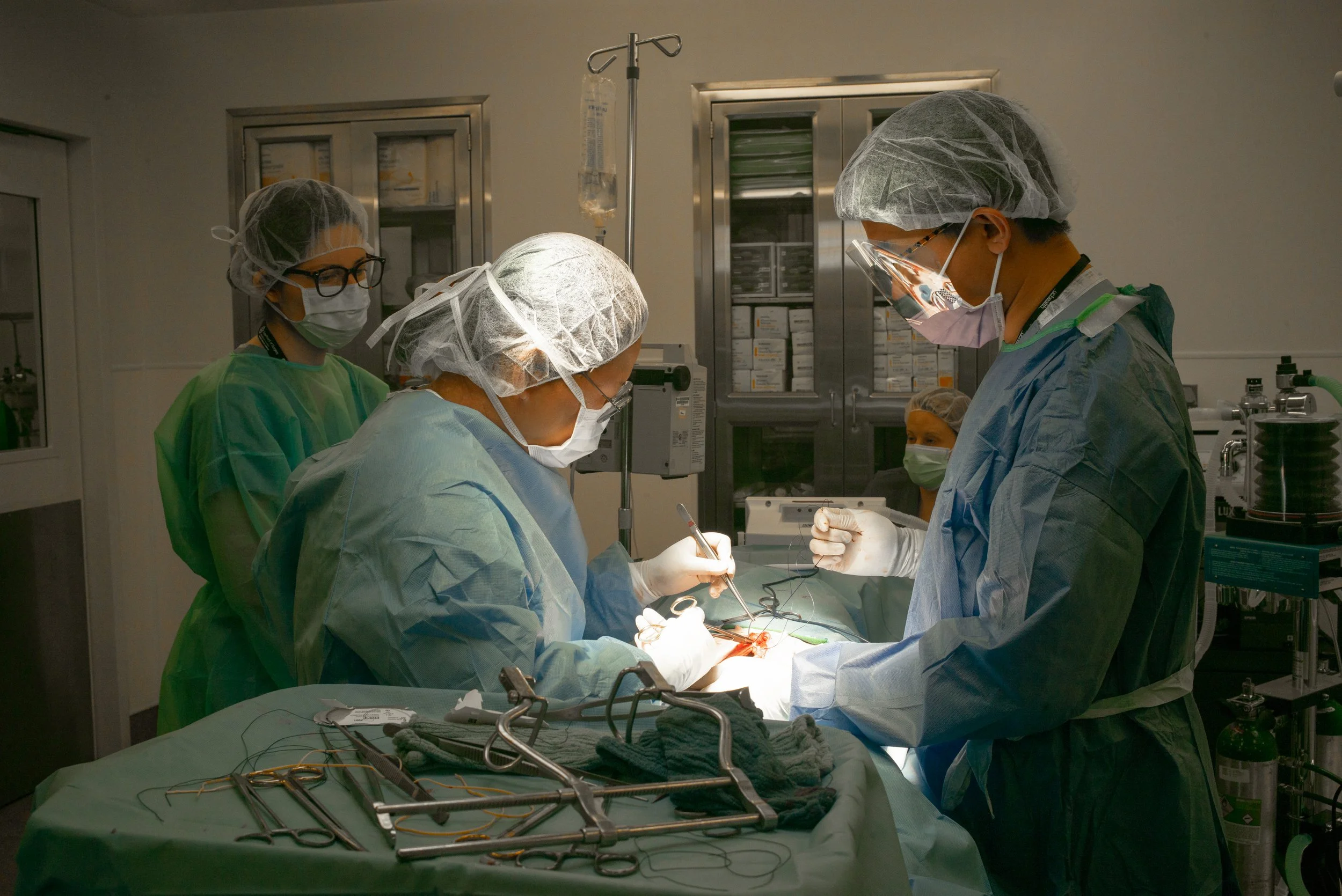 A team of medical professionals performing surgery in an operating room, wearing protective masks, gowns, and gloves.
