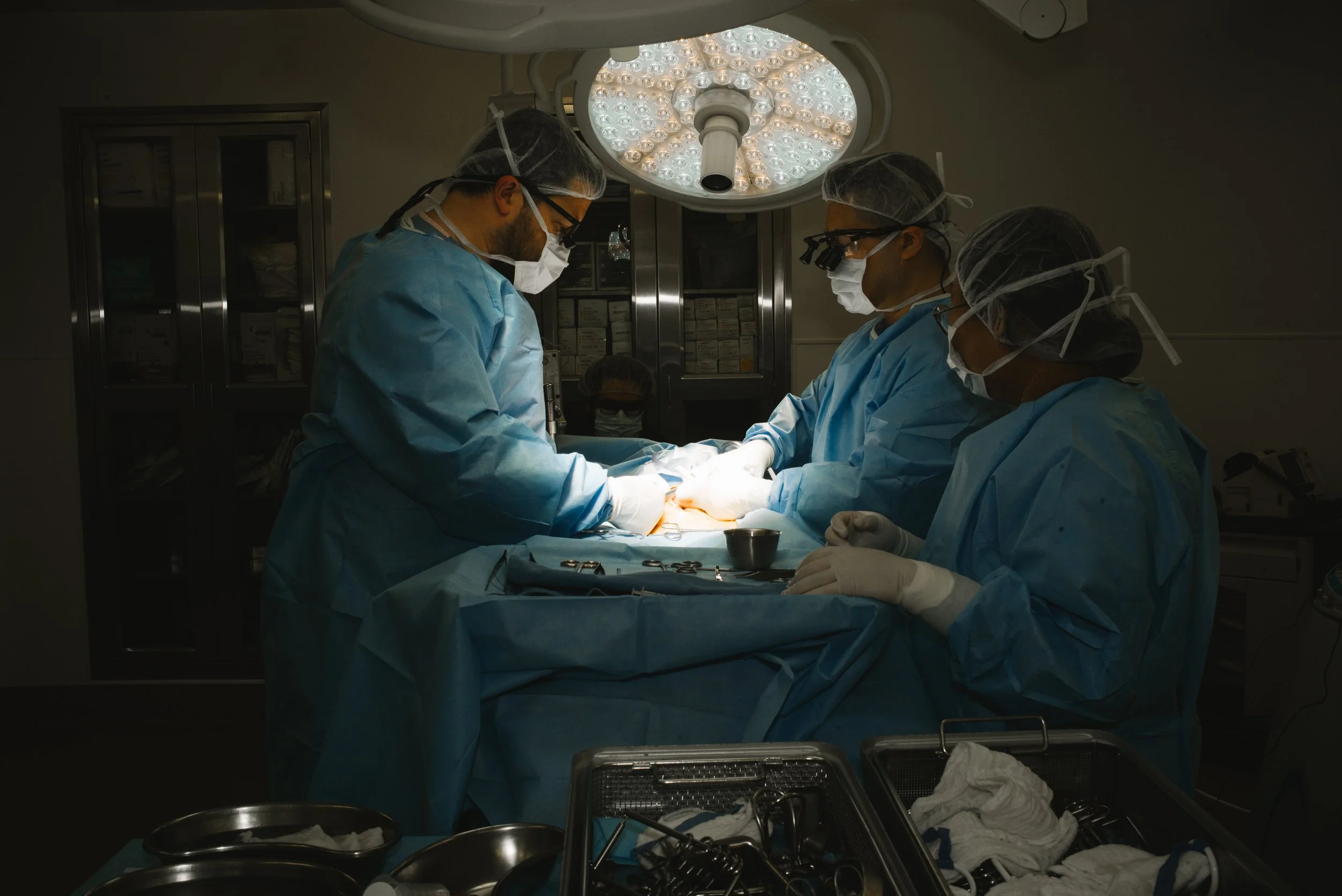 Medical team performing surgery in an operating room under bright surgical lights.