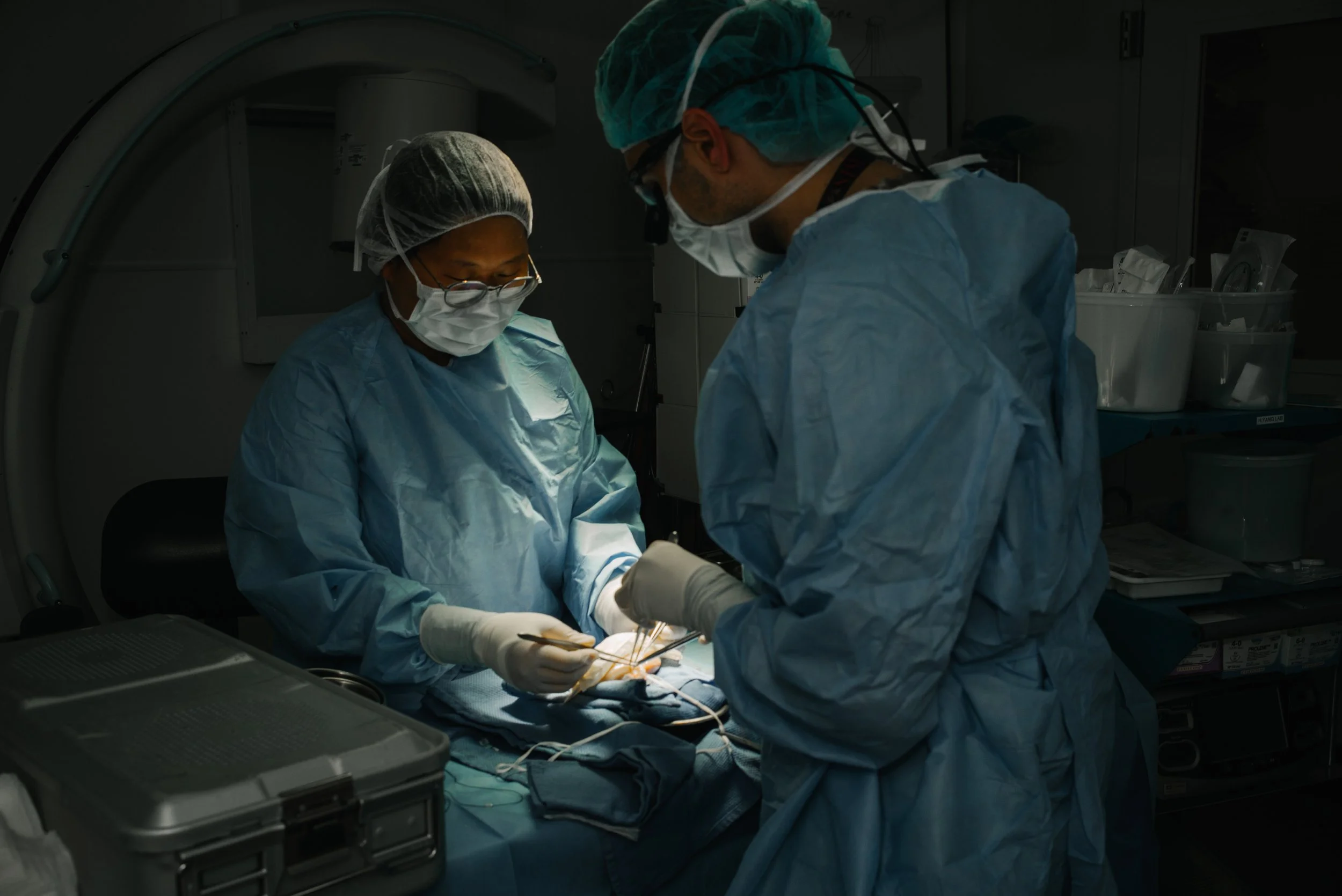 Two medical professionals in surgical gowns, masks, and gloves performing surgery in an operating room.